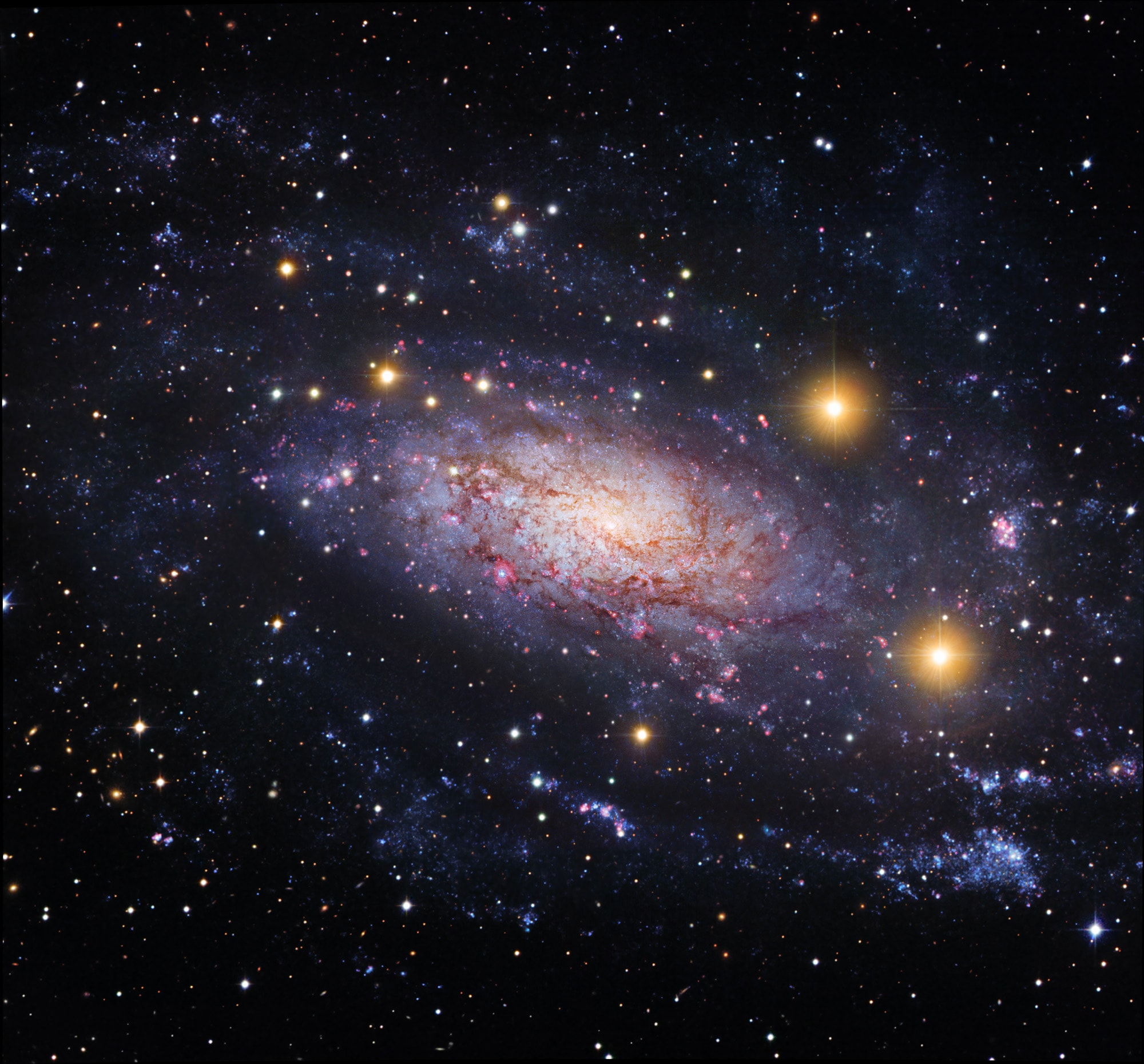 Far beyond the local group of galaxies lies NGC 3621, some 22 million light-years away. Found in the multi-headed southern constellation Hydra, the winding spiral arms of this gorgeous island universe are loaded with luminous blue star clusters, pinkish starforming regions, and dark dust lanes. Still, for astronomers NGC 3621 has not been just another pretty face-on spiral galaxy. Some of its brighter stars have been used as standard candles to establish important estimates of extragalactic distances and the scale of the Universe. This beautiful image of NGC 3621, is a composite of space- and ground-based telescope data. It traces the loose spiral arms far from the galaxy's brighter central regions for some 100,000 light-years. Spiky foreground stars in our own Milky Way Galaxy and even more distant background galaxies are scattered across the colorful skyscape.