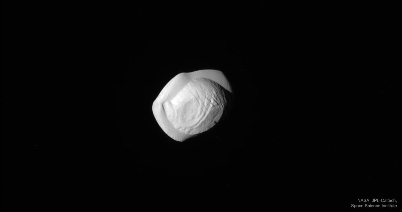 Why does Saturn's moon Pan look so odd? Images taken last week from the robotic Cassini spacecraft orbiting Saturn have resolved the moon in unprecedented detail.  The surprising images reveal a moon that looks something like a walnut with a slab through its middle.  Other visible features on Pan include rolling terrain, long ridges, and a few craters. Spanning 30-kilometer across, Pan orbits inside the 300-kilometer wide Encke Gap of Saturn's expansive A-ring, a gap known since the late 1800s.  Next month, Cassini will be directed to pass near Saturn's massive moon Titan so it can be pulled into a final series of orbits that will take it, on occasion, completely inside Saturn's rings and prepare it to dive into Saturn's atmosphere.