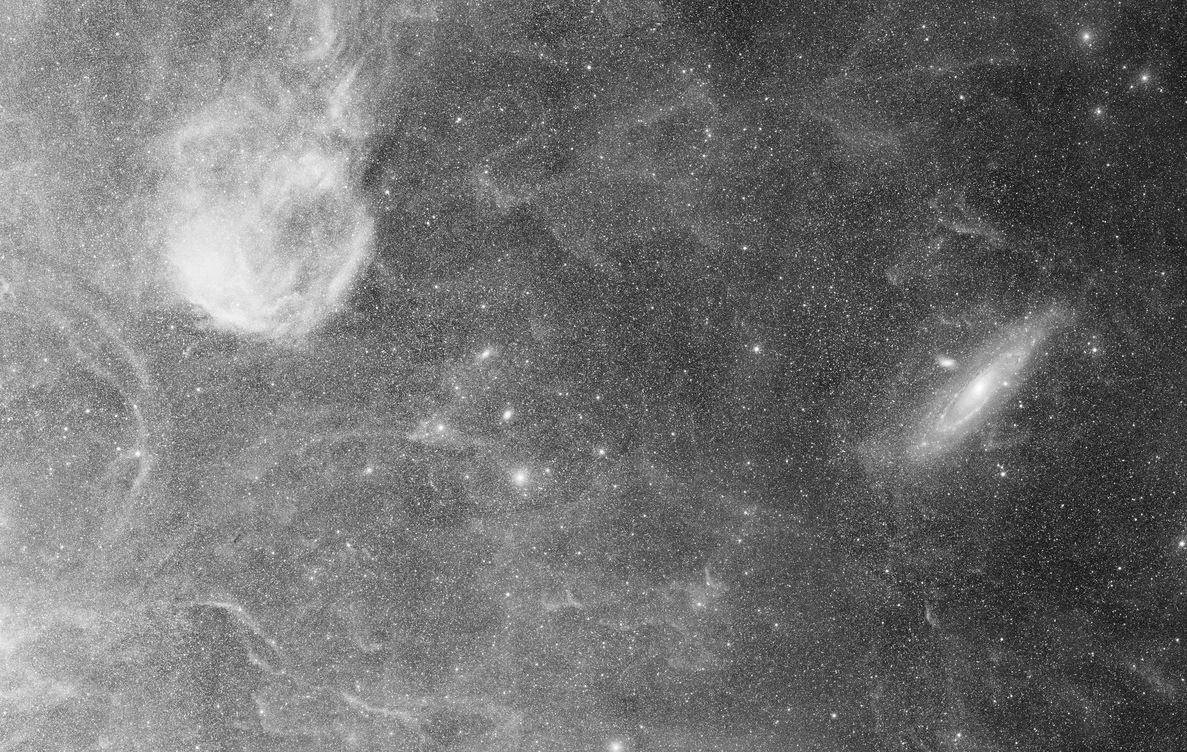 From within the boundaries of the constellation Cassiopeia (left) to Andromeda (right), this telescopic mosaic spans over 10 degrees in planet Earth's skies. The celestial scene is constructed of panels that are part of a high-resolution astronomical survey of the Milky Way in hydrogen-alpha light. Processing the monochromatic image data has brought out the region's faintest structures, relatively unexplored filaments of hydrogen gas near the plane of our Milky Way Galaxy. Large but faint and also relatively unknown nebula Sivan 2 is at the upper left in the field. The nearby Andromeda Galaxy, M31, is at center right, while the faint, pervasive hydrogen nebulosities stretch towards M31 across the foreground in the wide field of view. The broad survey image demonstrates the intriguing faint hydrogen clouds recently imaged by astronomer Rogelio Bernal Andreo really are within the Milky Way, along the line-of-sight to the Andromeda Galaxy.