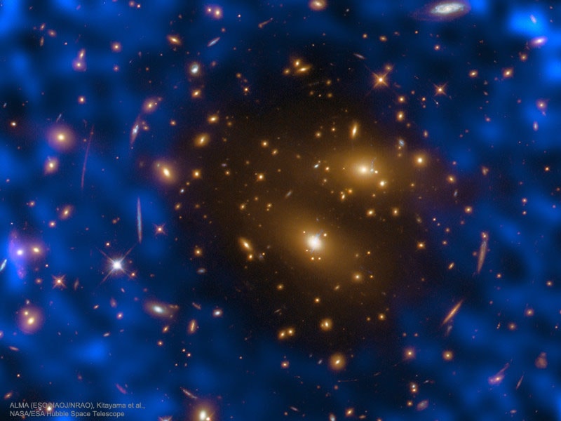 Why would this cluster of galaxy punch a hole in the cosmic microwave background (CMB)? First, the famous CMB was created by cooling gas in the early universe and flies right through most gas and dust in the universe. It is all around us. Large clusters of galaxies have enough gravity to contain very hot gas -- gas hot enough to up-scatter microwave photons into light of significantly higher energy, thereby creating a hole in CMB maps.  This Sunyaev�Zel'dovich (SZ) effect has been used for decades to reveal new information about hot gas in clusters and even to help discover galaxy clusters in a simple yet uniform way. Pictured is the most detailed image yet obtained of the SZ effect, now using both  ALMA to measure the CMB and the Hubble Space Telescope to measure the galaxies in the massive galaxy cluster RX J1347.5-1145.  False-color blue depicts light from the CMB, while almost every yellow object is a galaxy.  The shape of the SZ hole indicates not only that hot gas is present in this galaxy cluster, but also that it is distributed in a surprisingly uneven manner.