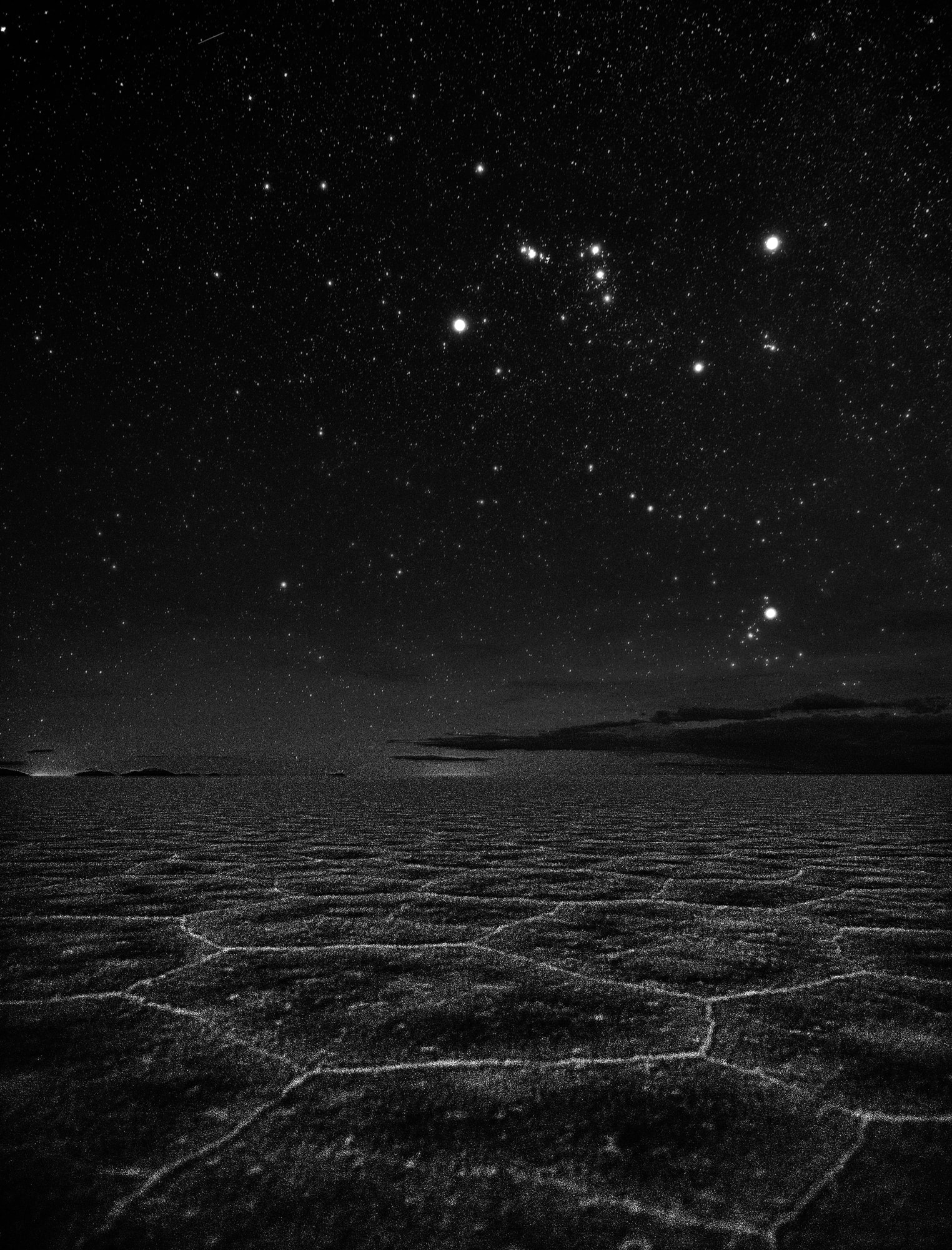 A scene in high contrast this thoughtful night skyscape is a modern composition inspired by M. C. Escher's lithograph Phosphorescent Sea. In it, bright familiar stars of Orion the Hunter and Aldebaran, eye of Taurus the Bull, hang in clear dark skies above a distant horizon. Below, faintly luminous edges trace an otherworldly constellation of patterns in mineral-crusted mud along the Uyuni Salt Flat of southwest Bolivia. The remains of an ancient lake, the Uyuni Salt Flat, Salar de Uyuni, is planet Earth's largest salt flat, located on the Bolivian Altiplano at an altitude of about 3,600 meters. Escher's 1933 lithograph also featured familiar stars in planet Earth's night, framing The Plough or Big Dipper above waves breaking on a more northern shore.