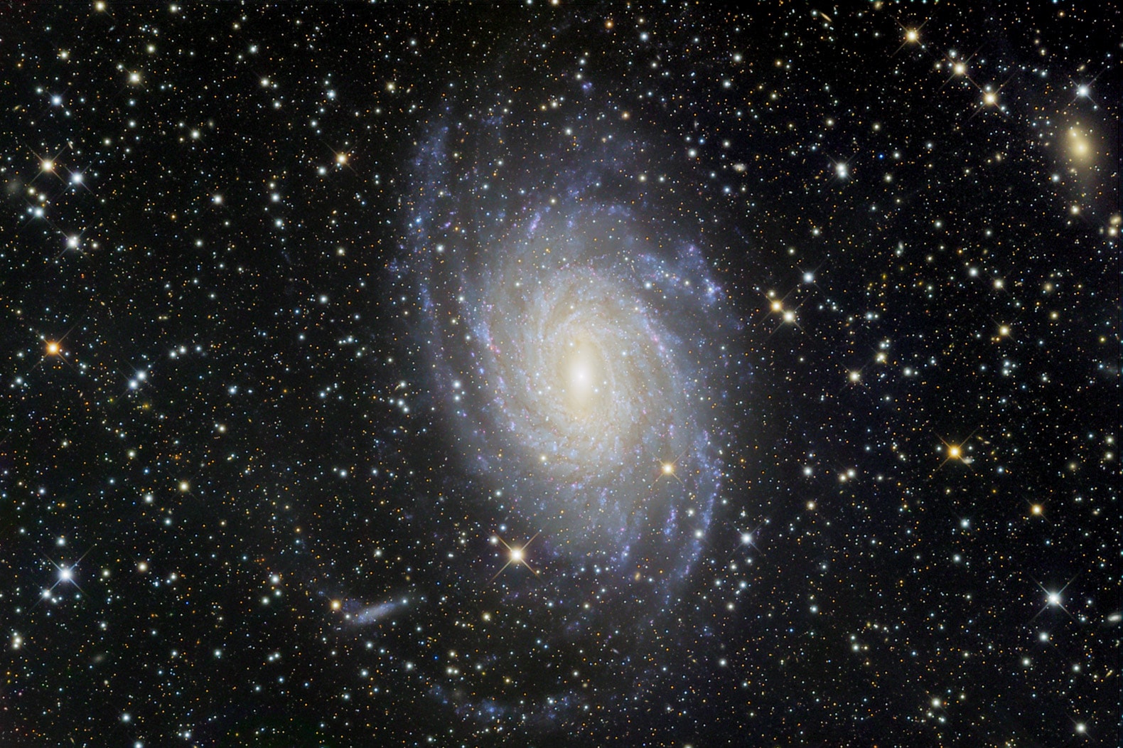 Big, beautiful spiral galaxy NGC 6744 is nearly 175,000 light-years across, larger than our own Milky Way. It lies some 30 million light-years distant in the southern constellation Pavo appearing as a faint, extended object in small telescopes. We see the disk of the nearby island universe tilted towards our line of sight. This remarkably distinct and detailed galaxy portrait covers an area about the angular size of the full moon. In it, the giant galaxy's yellowish core is dominated by the light from old, cool stars. Beyond the core, spiral arms filled with young blue star clusters and pinkish star forming regions sweep past a smaller satellite galaxy at the lower left, reminiscent of the Milky Way's satellite galaxy the Large Magellanic Cloud.
