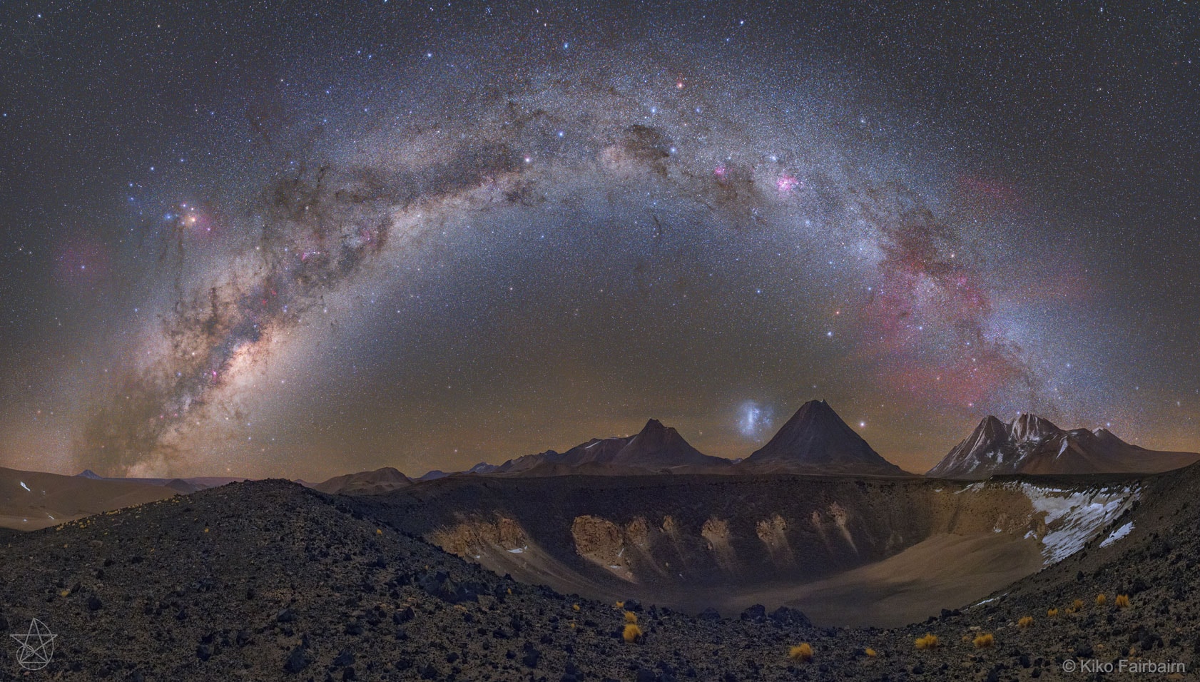Sometimes, the sky mimics the ground.  Taken in 2017 May from the Atacama Desert in Chile, the foreground of the featured image encompasses the dipping edge of the caldera of an extinct volcano. Poetically echoing the dip below is the arch of our Milky Way Galaxy above.  Many famous icons dot this southern nighttime vista, including the center of our Milky Way Galaxy on the far left, the bright orange star Antares also on the left, the constellation of the Southern Cross near the top of the arch, and the red-glowing Gum Nebula on the far right. Just above the horizon and splitting two distant volcanic peaks near the image center is the Large Magellanic Cloud -- the largest satellite galaxy of the Milky Way.    Today's Total Solar Eclipse: Live NASA Streaming Video