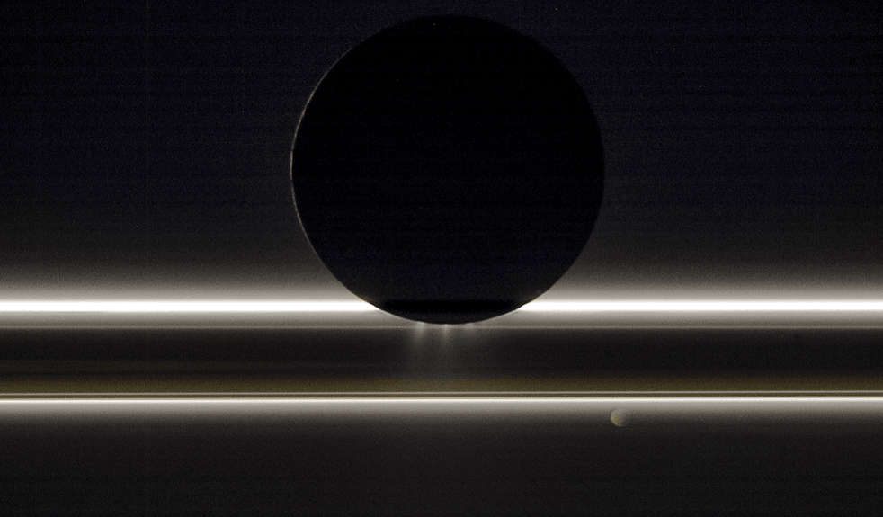 One of our Solar System's most tantalizing worlds, Enceladus is backlit by the Sun in this Cassini spacecraft image from November 1, 2009. The dramatic illumination reveals the plumes that continuously spew into space from the south pole of Saturn's 500 kilometer diameter moon. Discovered by Cassini in 2005, the icy plumes are likely connected to an ocean beneath the ice shell of Enceladus. They supply material directly to Saturn's outer, tenuous E ring and make the surface of Enceladus as reflective as snow. Across the scene, Saturn's icy rings scatter sunlight toward Cassini's cameras. Beyond the rings, the night side of 80 kilometer diameter moon Pandora is faintly lit by Saturnlight.