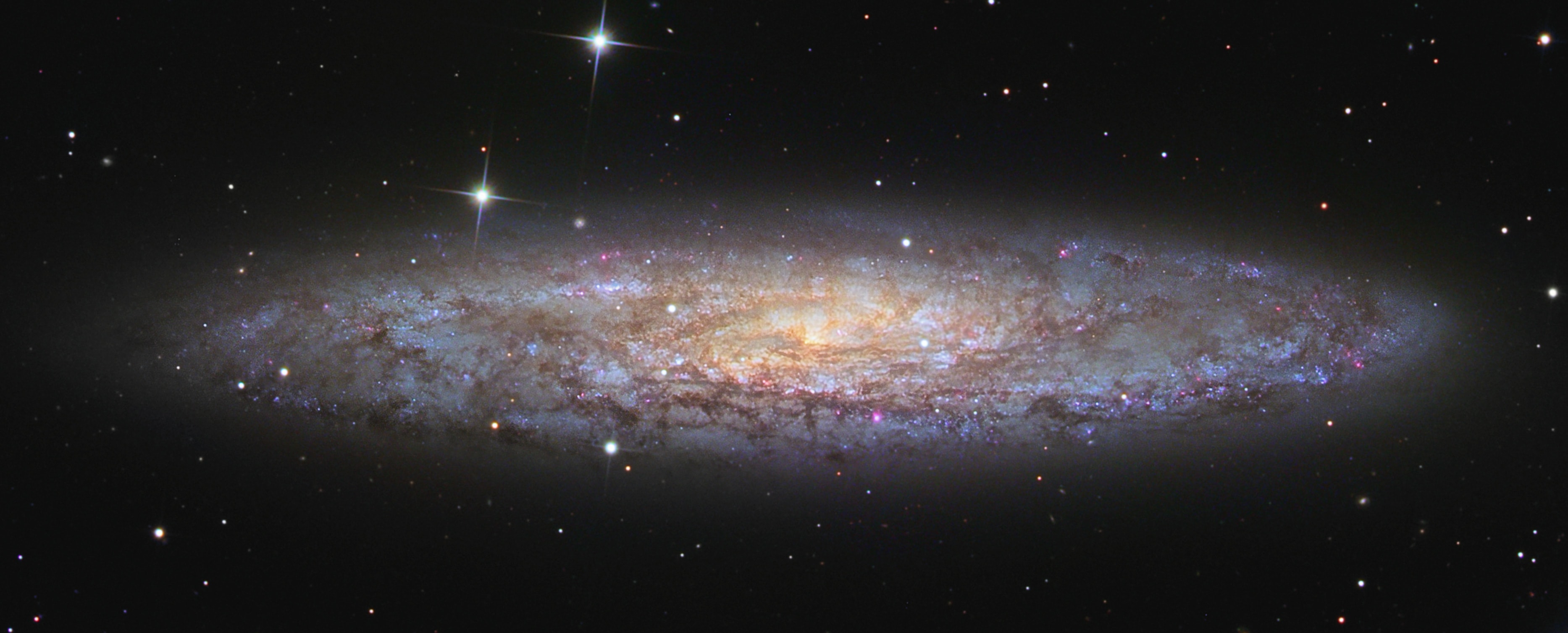 Shiny NGC 253 is one of the brightest spiral galaxies visible, and also one of the dustiest.  Some call it the Silver Dollar Galaxy for its appearance in small telescopes, or just the Sculptor Galaxy for its location within the boundaries of the southern constellation Sculptor.  Discovered in 1783 by mathematician and astronomer Caroline Herschel, the dusty island universe lies a mere 10 million light-years away. About 70 thousand light-years across, NGC 253 is the largest member of the Sculptor Group of Galaxies, the nearest to our own Local Group of Galaxies.  In addition to its spiral dust lanes, tendrils of dust seem to be rising from a galactic disk laced with young star clusters and star forming regions in this sharp color image. The high dust content accompanies frantic star formation, earning NGC 253 the designation of a starburst galaxy. NGC 253 is also known to be a strong source of high-energy x-rays and gamma rays, likely due to massive black holes near the galaxy's center. Take a trip through extragalactic space in this short video flyby of NGC 253.