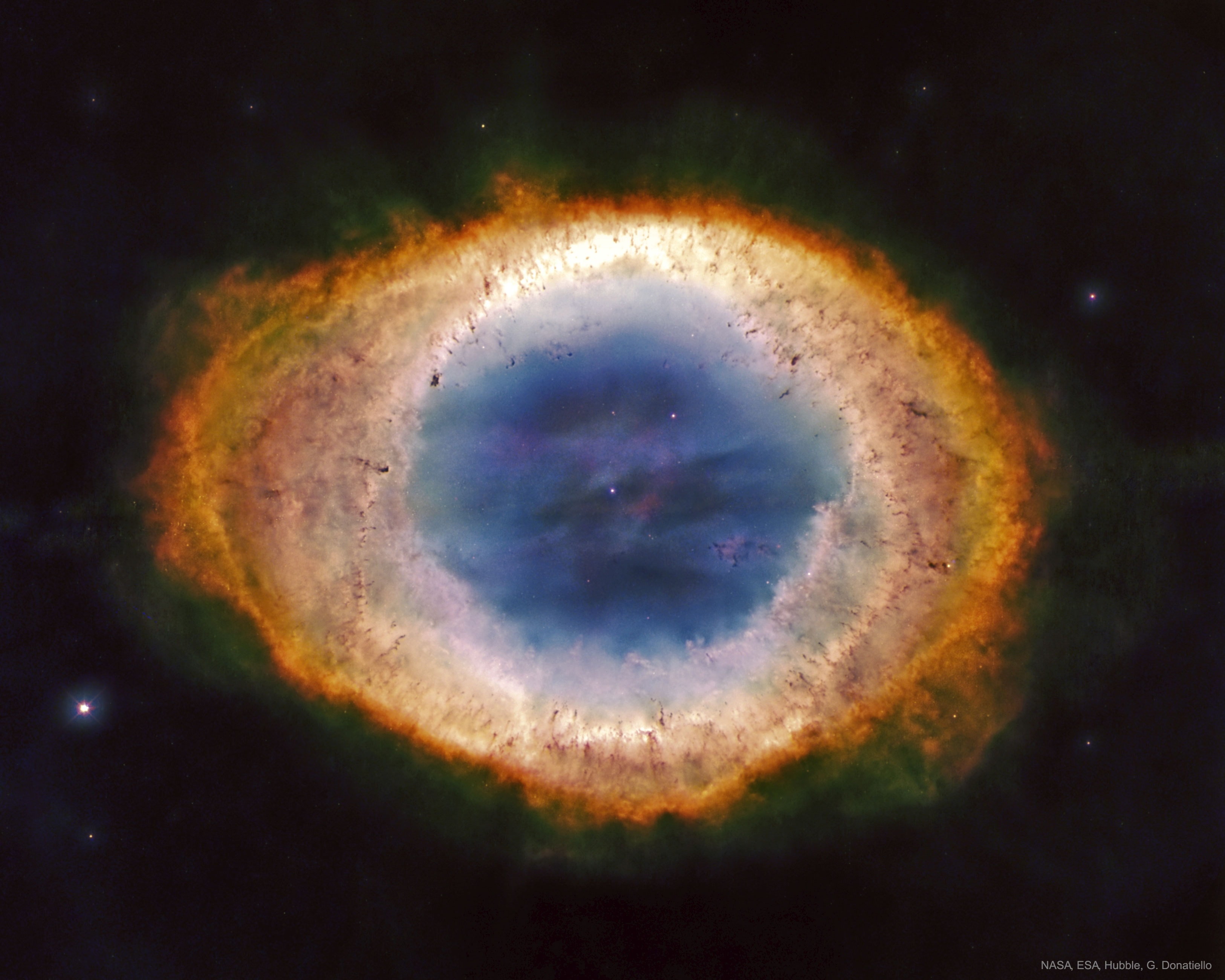 cept for the rings of Saturn, the Ring Nebula (M57) is probably the most famous celestial band. Its classic appearance is understood to be due to our own perspective, though. The recent mapping of the expanding nebula's 3-D structure, based in part on this clear Hubble image,indicates that the nebula is a relatively dense, donut-like ring wrapped around the middle of a (American) football-shaped cloud of glowing gas. The view from planet Earth looks down the long axis of the football, face-on to the ring. Of course, in this well-studied example of a planetary nebula, the glowing material does not come from planets. Instead, the gaseous shroud represents outer layers expelled from the dying, once sun-like star, now a tiny pinprick of light seen at the nebula's center. Intense ultraviolet light from the hot central star ionizes atoms in the gas. The Ring Nebula is about one light-year across and 2,000 light-years away.   Share the Sky: NASA Open API for APOD