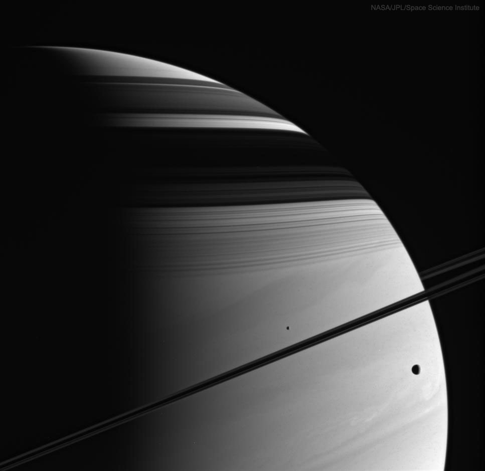 While cruising around Saturn, be on the lookout for picturesque juxtapositions of moons, rings, and shadows. One quite picturesque arrangement occurred in 2005 and was captured by the then Saturn-orbiting Cassini spacecraft. In the featured image, moons Tethys and Mimas are visible on either side of Saturn's thin rings, which are seen nearly edge-on.  Across the top of Saturn are dark shadows of the wide rings, exhibiting their impressive complexity. The violet-light image brings up the texture of the backdrop: Saturn's clouds. Cassini orbited Saturn from 2004 until September of last year, when the robotic spacecraft was directed to dive into Saturn to keep it from contaminating any moons.