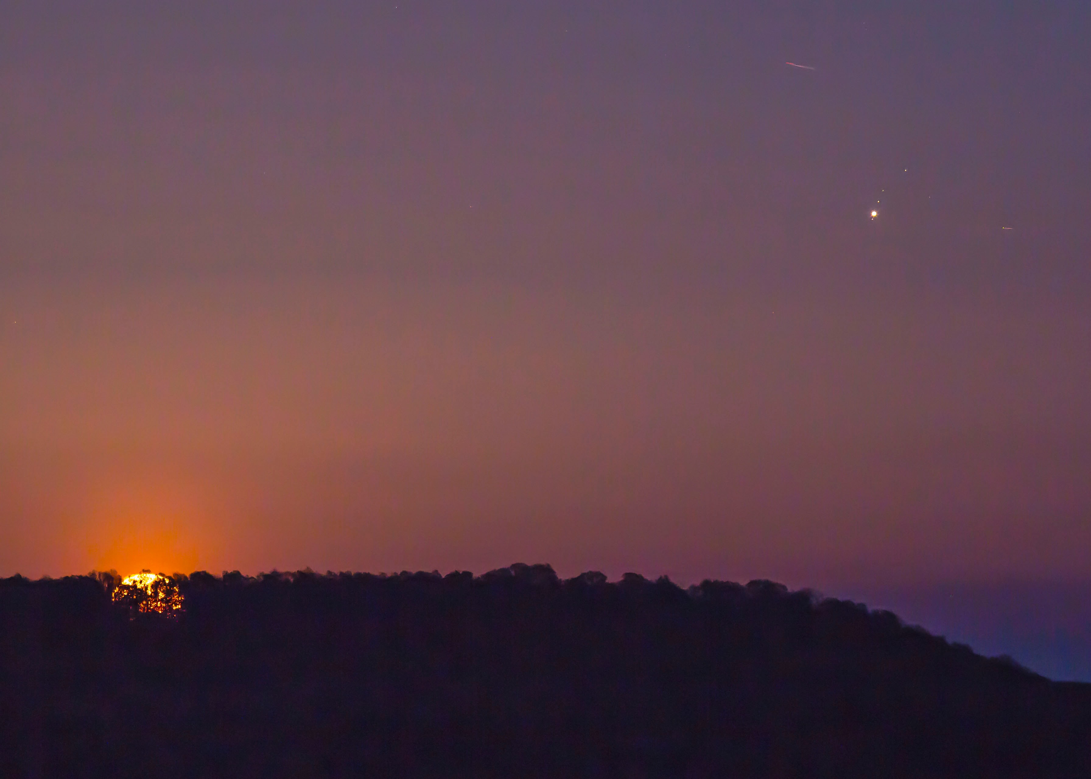 On April 30, a Full Moon rose opposite the setting Sun. Its yellowish moonglow silhouettes a low tree-lined ridge along Lewis Mountain in this northeastern Alabama skyscape. Sharing the telephoto field-of-view opposite the Sun are Earth's grey shadow, the pinkish Belt of Venus, and bright planet Jupiter. Nearing its own 2018 opposition on May 8, Jupiter is flanked by tiny pinpricks of light, three of its large Galilean moons. Europa lies just below Jupiter, and Ganymede and Callisto are just above. Closer and brighter, our own natural satellite appears to loom large but the Moon is physically a little smaller than Ganymede and Callisto, and slightly larger than water world Europa. Sharp eyes will also spot the trails of two jets across the clear evening sky.