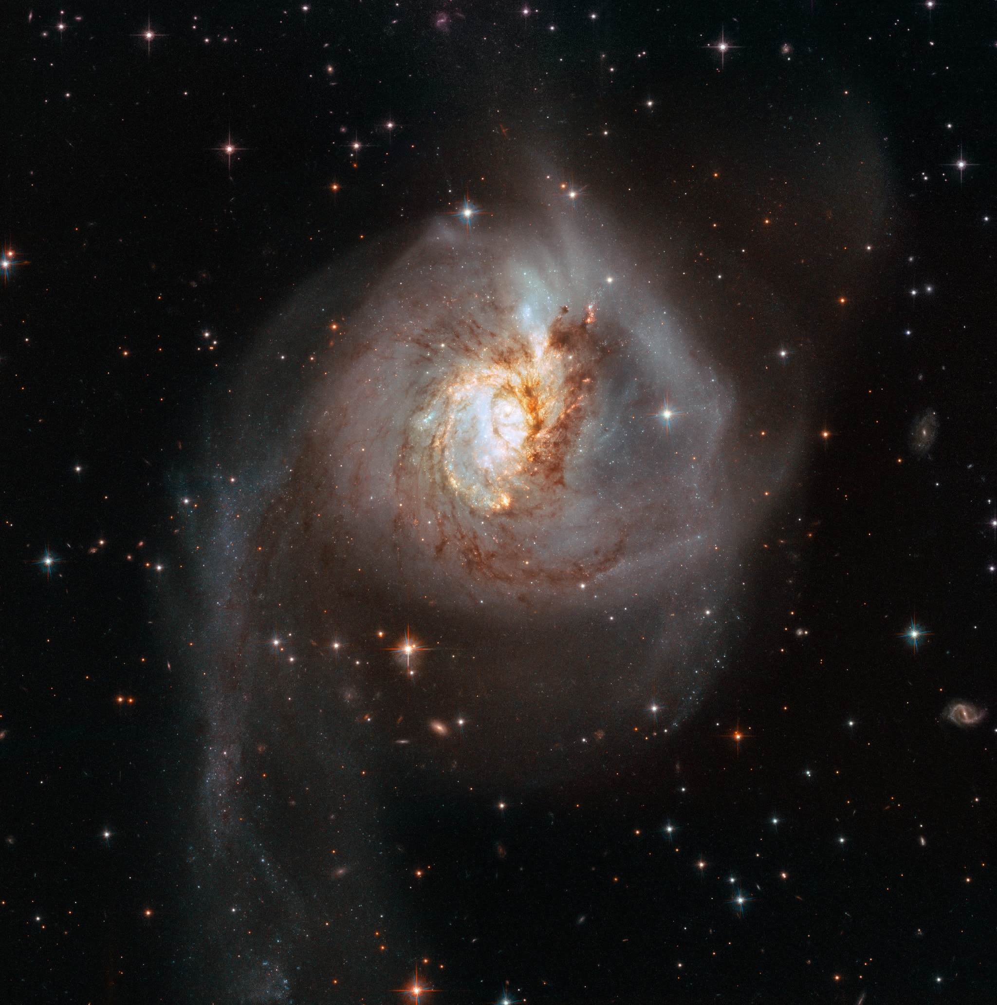 Marked by an unusually bright central region, swirling dust lanes, and far flung tidal tails, peculiar NGC 3256 is the aftermath of a truly cosmic collision. The 500 million year old clash of two separate galaxies spans some 100 thousand light-years in this sharp Hubble view. Of course when two galaxies collide, individual stars rarely do. Giant galactic clouds of molecular gas and dust do interact though, and produce spectacular bursts of star formation. In this galaxy clash, the two original spiral galaxies had similar masses. Their disks are no longer distinct and the two galactic nuclei are hidden by obscuring dust. On the timescale of a few hundred million years the nuclei will likely also merge as NGC 3256 becomes a single large elliptical galaxy. NGC 3256 itself is nearly 100 million light-years distant toward the southern sailing constellation Vela. The frame includes many even more distant background galaxies and spiky foreground stars.
