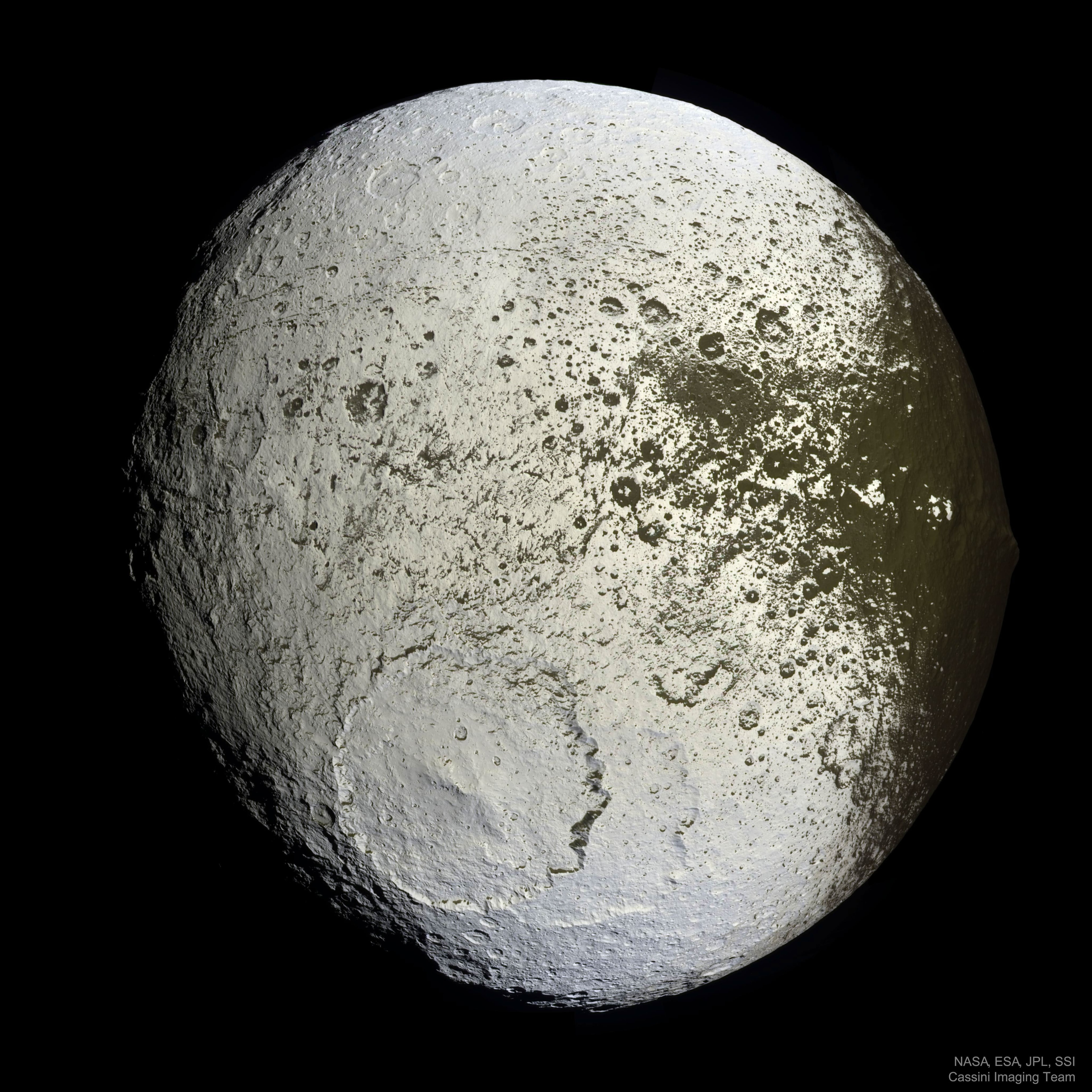 What has happened to Saturn's moon Iapetus?  Vast sections of this strange world are dark as coal, while others are as bright as ice.  The composition of the dark material is unknown, but infrared spectra indicate that it possibly contains some dark form of carbon. Iapetus also has an unusual equatorial ridge that makes it appear like a walnut.  To help better understand this seemingly painted moon, NASA directed the robotic Cassini spacecraft orbiting Saturn to swoop within 2,000 kilometers in 2007. Pictured here, from about 75,000 kilometers out, Cassini's trajectory allowed unprecedented imaging of the hemisphere of Iapetus that is always trailing.  A huge impact crater seen in the south spans a tremendous 450 kilometers and appears superposed on an older crater of similar size. The dark material is seen increasingly coating the easternmost part of Iapetus, darkening craters and highlands alike.  Close inspection indicates that the dark coating typically faces the moon's equator and is less than a meter thick. A leading hypothesis is that the dark material is mostly dirt leftover when relatively warm but dirty ice sublimates. An initial coating of dark material may have been effectively painted on by the accretion of meteor-liberated debris from other moons.
