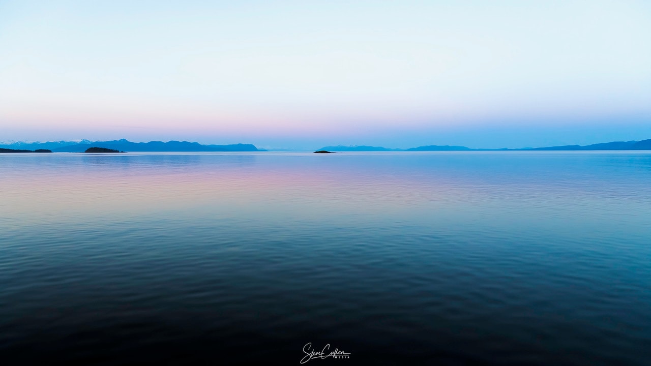 At sunset look east not west. As Earth's dark shadow rises from the eastern horizon, faint and subtle colors will appear opposite the setting Sun. This beautiful evening sea and skyscape records the reflective scene from a cruise on the well-traveled Alaskan Inside Passage in the Pacific Northwest. Along the horizon the fading sunset gives way to the pinkish anti-twilight arch, more poetically known as the Belt of Venus. Often overlooked at sunset in favor of the brighter western horizon, the lovely arch is tinted by filtered sunlight backscattered in the dense atmosphere, hugging the planet's rising blue-grey shadow.