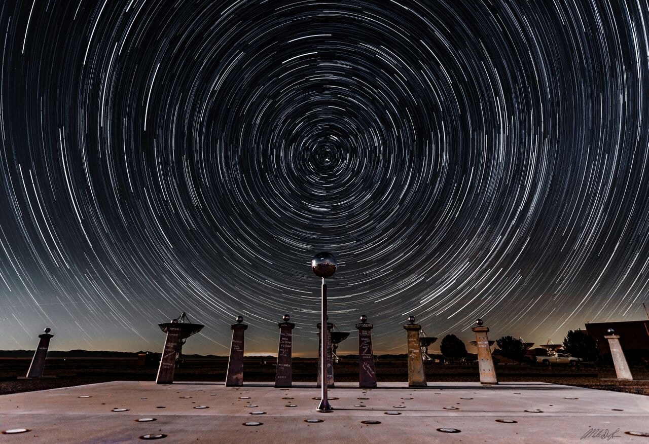 Sundials use the location of a shadow to measure the Earth's rotation and indicate the time of day. So it's fitting that this sundial, at the Very Large Array Radio Telescope Observatory in New Mexico, commemorates the history of radio astronomy and radio astronomy pioneer Ronald Bracewell. The radio sundial was constructed using pieces of a solar mapping radio telescope array that Bracewell orginaly built near the Stanford University campus. Bracewell's array was used to contribute data to plan the first Moon landing,  its pillars signed by visiting scientists and radio astronomers, including two Nobel prize winners. As for most sundials the shadow cast by the central gnomon follows markers that show the solar time of day, along with solstices and equinoxes. But markers on the radio sundial are also laid out according to local sidereal time. They show the position of the invisible radio shadows of three bright radio sources in Earth's sky, supernova remnant Cassiopeia A, active galaxy Cygnus A, and active galaxy Centaurus A. Sidereal time is just star time, the Earth's rotation as measured with the stars and distant galaxies. That rotation is reflected in this composited hour-long exposure. Above the Bracewell Radio Sundial, the stars trace concentric trails around the north celestial pole.