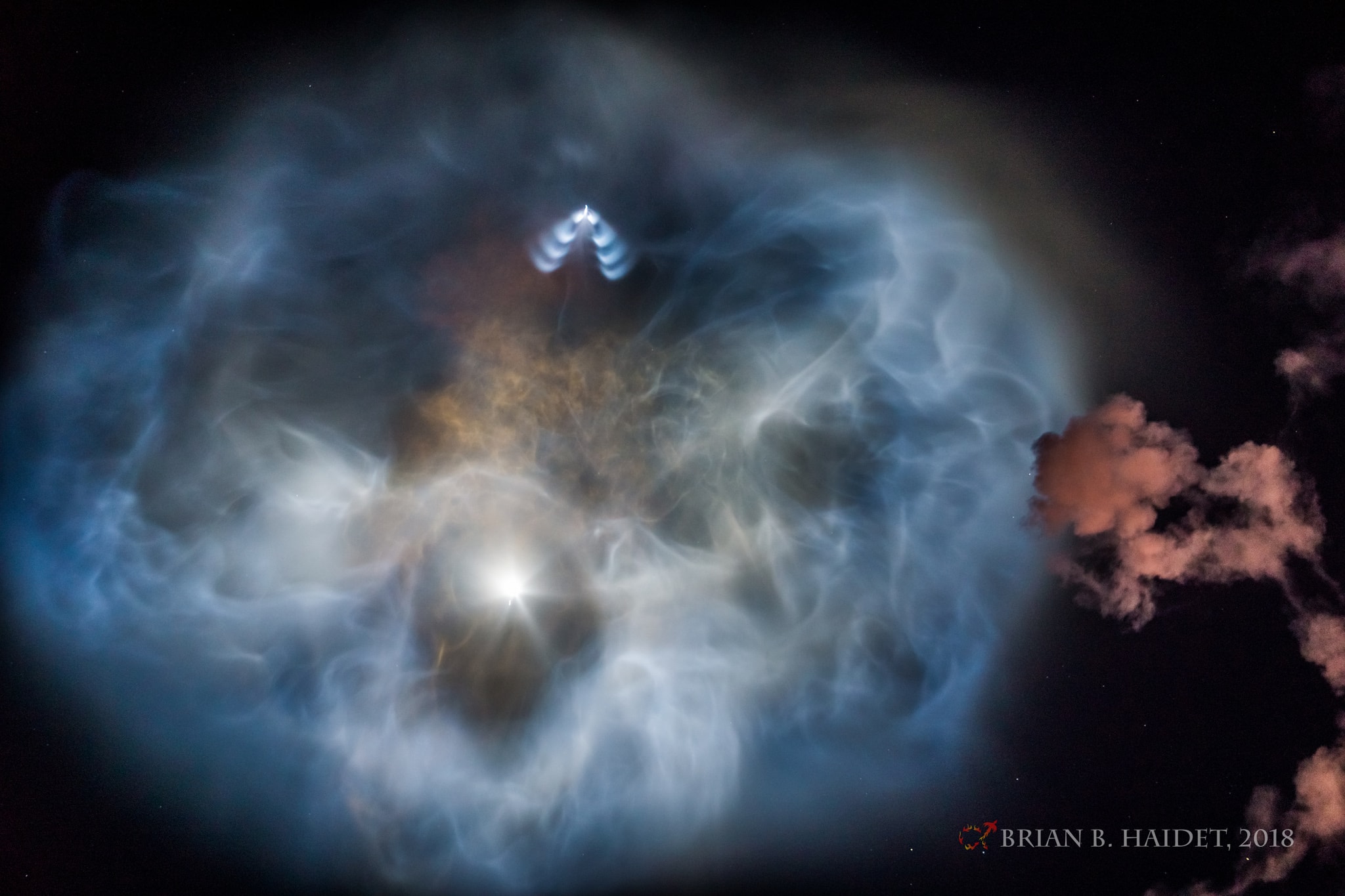 Not the Hubble Space Telescope's latest view of a distant planetary nebula, this illuminated cloud of gas and dust dazzled even casual U.S. west coast skygazers on October 7. Taken about three miles north of Vandenberg Air Force Base, the image follows plumes and exhaust from the first and second stage of a SpaceX Falcon 9 rocket rising through southern California's early evening skies. In the fading twilight, the reddish smoke drifting in the foreground at the right is from the initial ascent of the rocket. The expanding blue and orange filamentary plumes are from first and second stage separation and the first stage boostback burn, still in sunlight at extreme altitudes. But the bright spot below center is the second stage itself headed almost directly away from the camera, accelerating to orbital velocity and far downrange. Pulsed thrusters form the upside down V-shape at the top as they guide the reusable Falcon 9 first stage back to the landing site.