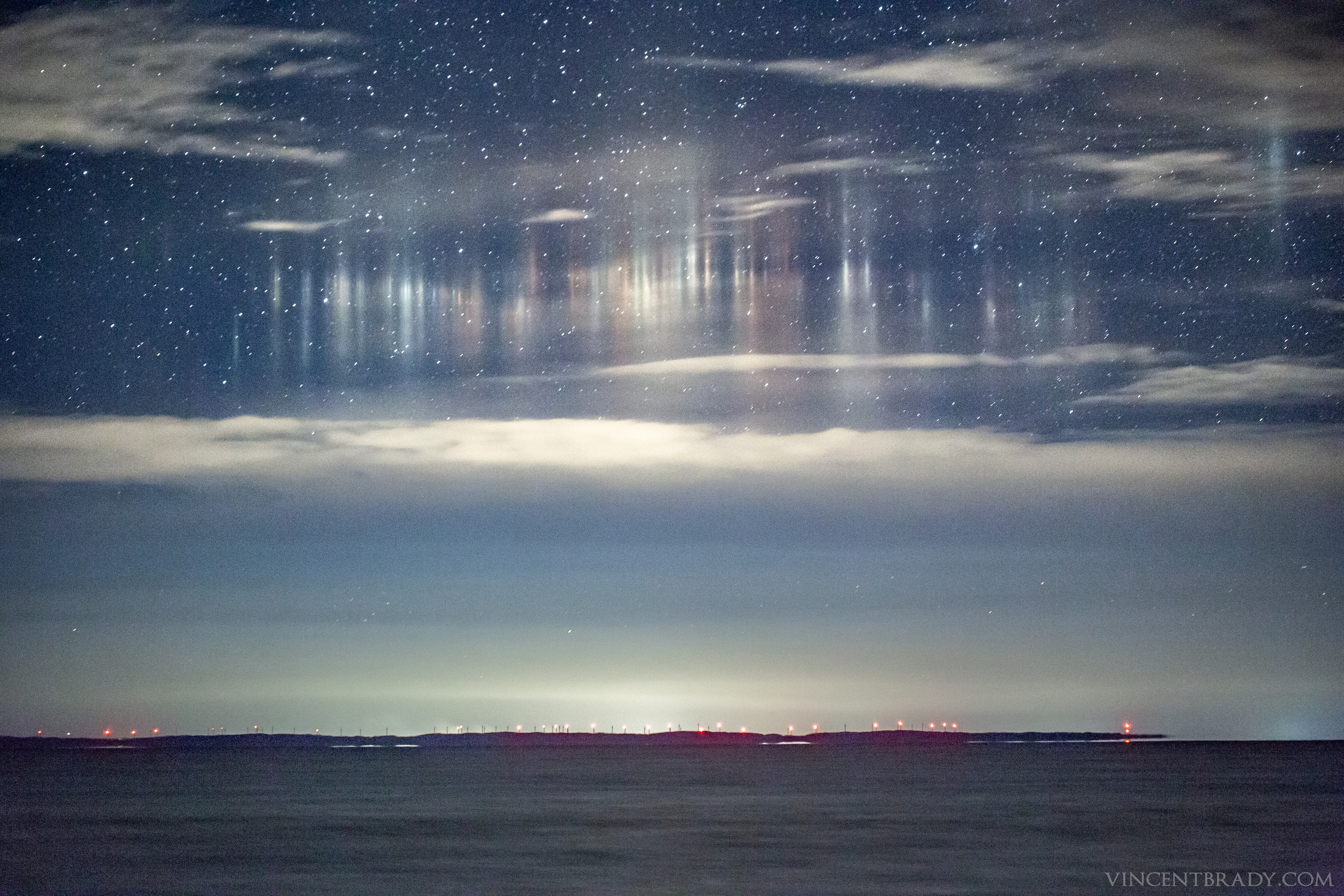 What's happening in the sky? Unusual lights appeared last week to hover above Whitefish Bay on the eastern edge of Lake Superior between the USA and Canada. Unsure of the cause, the Michigan-based astrophotographer switched camera lenses -- from fisheye to telephoto -- and soon realized he was seeing light pillars: vertical lines of light over a ground source that reflect from falling ice crystals.  As the ground temperature was above freezing, the flat crystals likely melted as they approached the ground, creating a lower end to the vertical light pillars.  The red ground lights originated from wind turbines on Ile Parisienne, a Canadian Island visible across the bay.