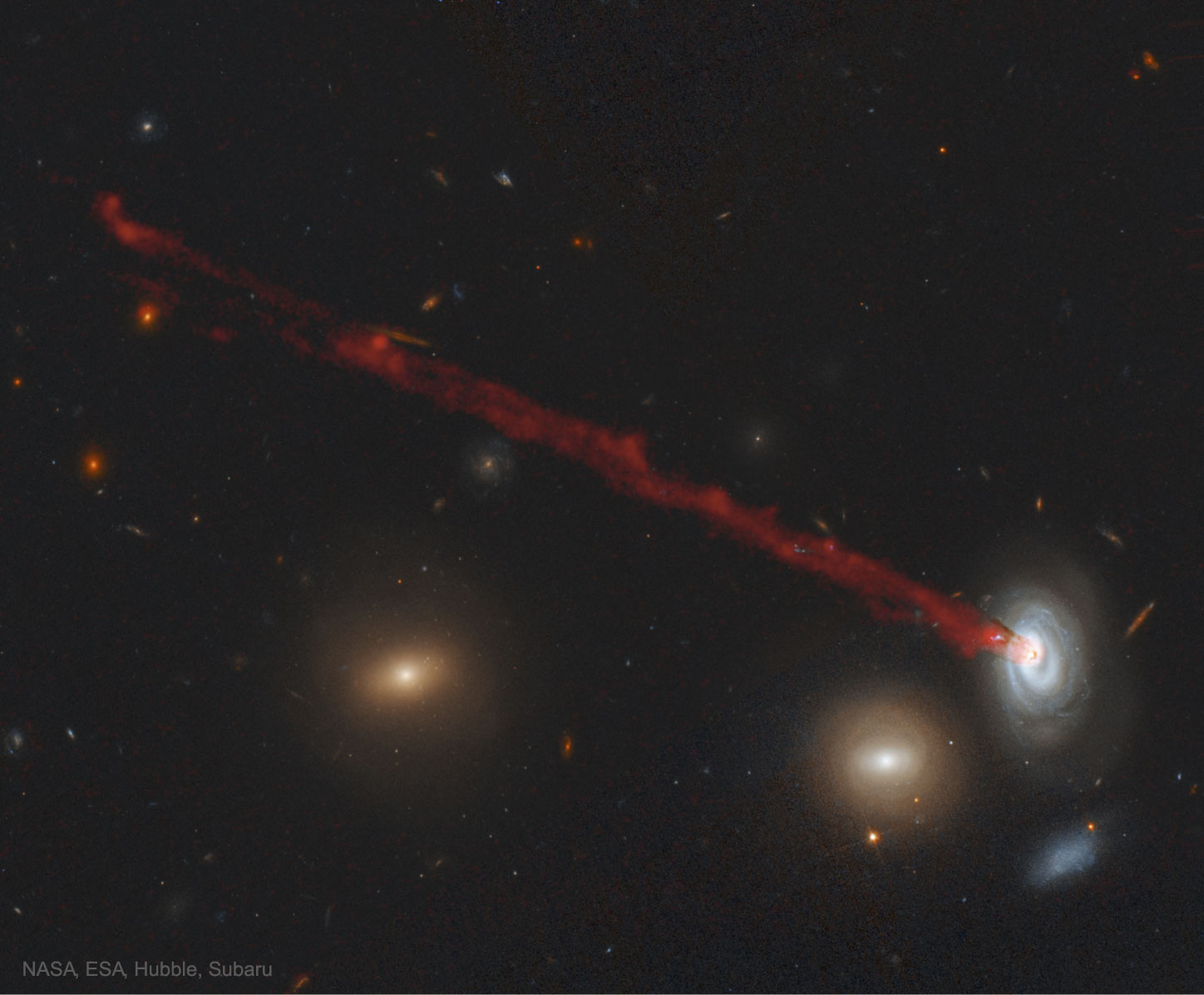 Why is there long red streak attached to this galaxy?  The streak is made mostly of glowing hydrogen that has been systematically stripped away as the galaxy moved through the ambient hot gas in a cluster of galaxies.  Specifically, the galaxy is spiral galaxy D100, and cluster is the Coma Cluster of galaxies.  The red path connects to the center of D100 because the outer gas, gravitationally held less strongly, has already been stripped away by ram pressure. The extended gas tail is about 200,000 light-years long, contains about 400,000 times the mass of our Sun, and stars are forming within it.  Galaxy D99, visible to D100's lower left, appears red because it glows primarily from the light of old red stars -- young blue stars can no longer form because D99 has been stripped of its star-forming gas. The featured false-color picture is a digitally enhanced composite of images from Earth-orbiting Hubble and the ground-based Subaru telescope. Studying remarkable systems like this bolsters our understanding of how galaxies evolve in clusters.