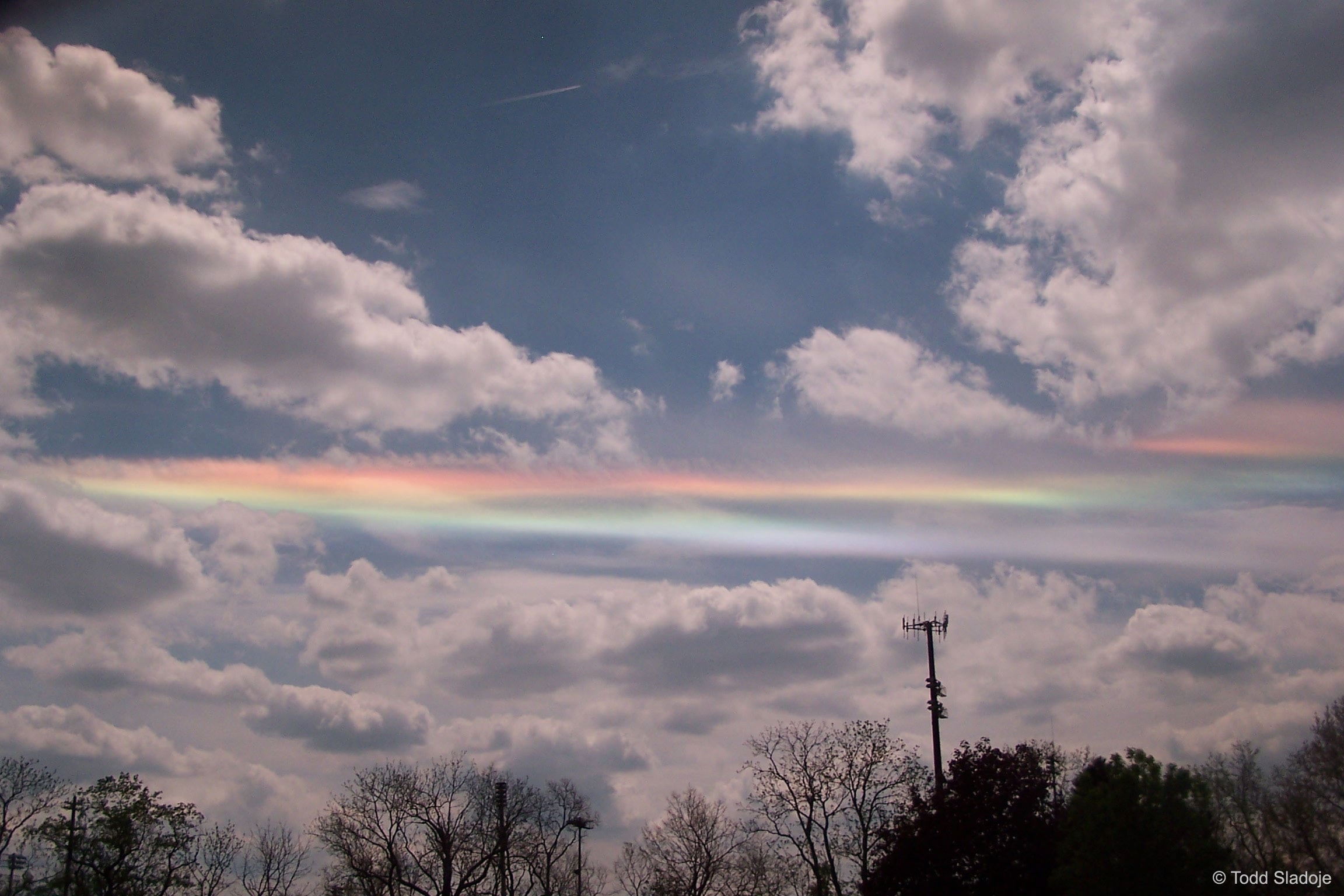 Why would clouds appear to be different colors? The reason here is that ice crystals in distant cirrus clouds are acting like little floating prisms.  Sometimes known as a fire rainbow for its flame-like appearance, a circumhorizon arc lies parallel to the horizon. For a circumhorizontal arc to be visible, the Sun must be at least 58 degrees high in a sky where cirrus clouds are present.  Furthermore, the numerous, flat, hexagonal ice-crystals that compose the cirrus cloud must be aligned horizontally to properly refract sunlight in a collectively similar manner.  Therefore, circumhorizontal arcs are quite unusual to see.  This circumhorizon display was photographed through a polarized lens above Dublin, Ohio in 2009.
