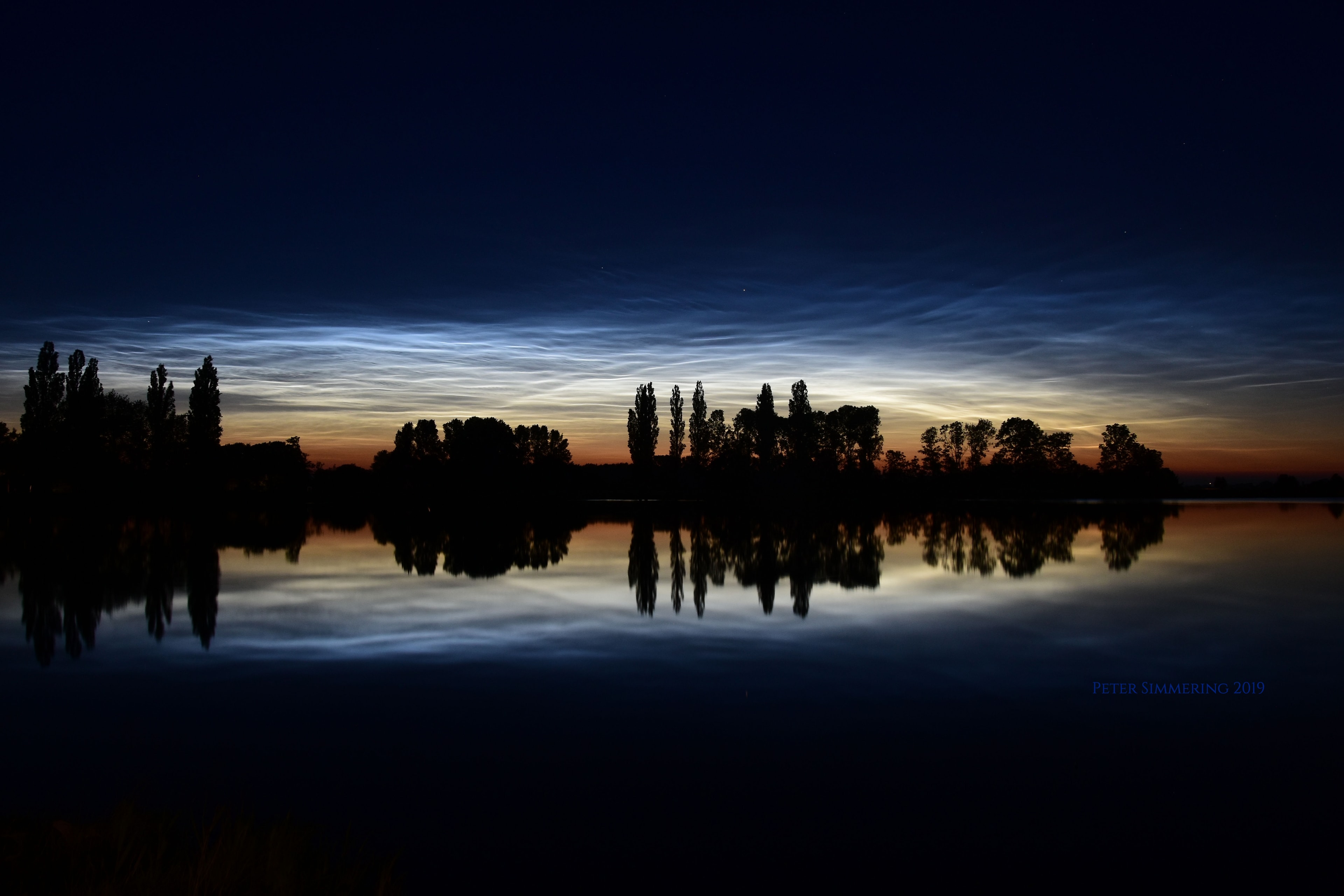 Sometimes it's night on the ground but day in the air. As the Earth rotates to eclipse the Sun, sunset rises up from the ground. Therefore, at sunset on the ground, sunlight still shines on clouds above.  Under usual circumstances, a pretty sunset might be visible, but unusual noctilucent clouds float so high up they can be seen well after dark.  Normally too dim to be seen, they may become visible just after sunset during the summer when illuminated by sunlight from below.  Noctilucent clouds are the highest clouds known and thought to be part of polar mesospheric clouds.  Featured here as they appeared two weeks ago, a network of noctilucent clouds was captured not only in the distant sky but in reflection from a small lake just north of Zwolle, Netherlands, with trees in stark silhouette across the horizon.  Unusually bright noctilucent clouds continue to appear over much of northern Europe.  Much about noctilucent clouds has been discovered only over the past decade, while how they form and evolve remains a topic of active research.    Gallery: Recent noctilucent clouds over Europe