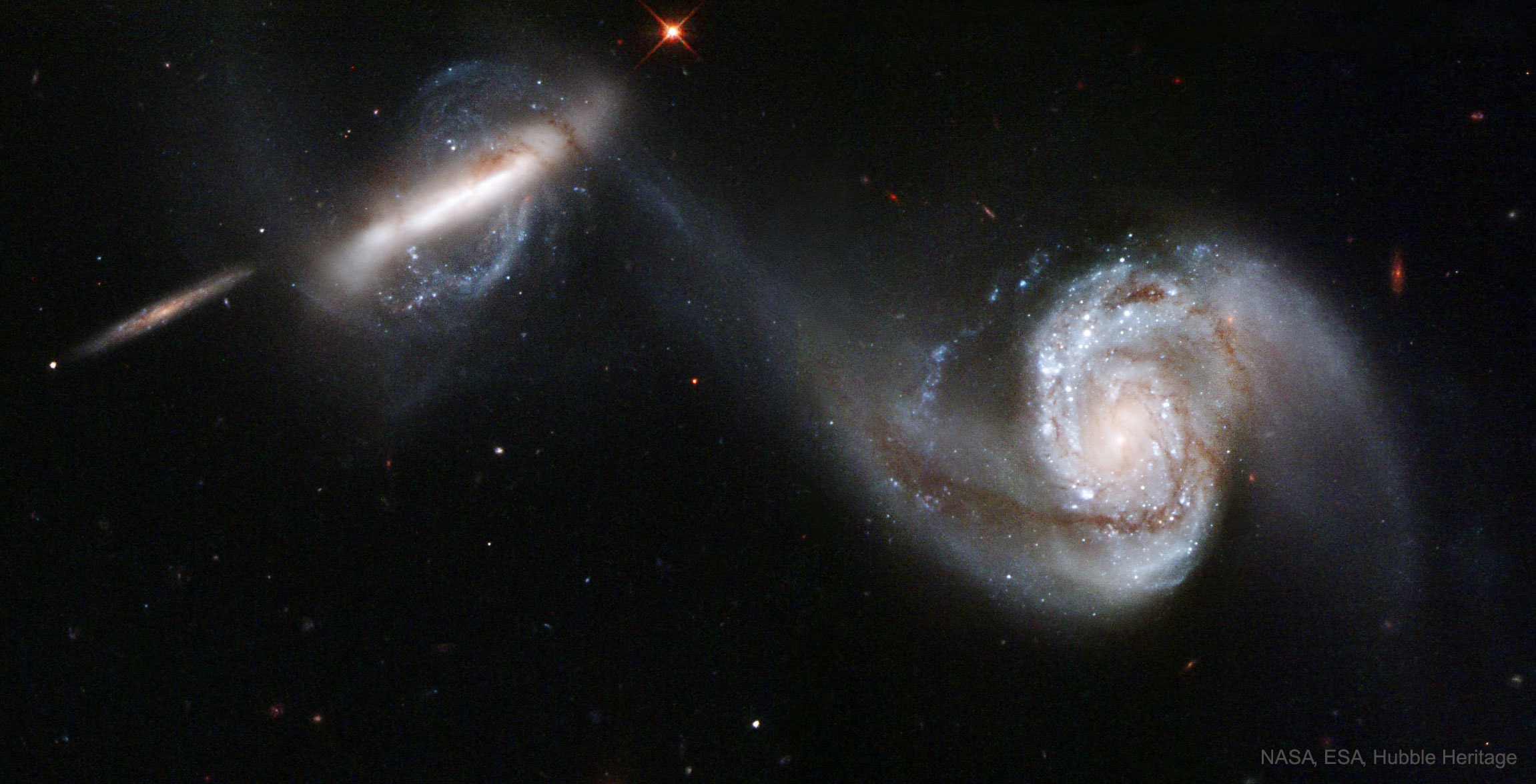 This dance is to the death.  Along the way, as these two large galaxies duel, a cosmic bridge of stars, gas, and dust currently stretches over 75,000 light-years and joins them.  The bridge itself is strong evidence that these two immense star systems have passed close to each other and experienced violent tides induced by mutual gravity. As further evidence, the face-on spiral galaxy on the right, also known as NGC 3808A, exhibits many young blue star clusters produced in a burst of star formation. The twisted edge-on spiral on the left (NGC 3808B) seems to be wrapped in the material bridging the galaxies and surrounded by a curious polar ring. Together, the system is known as Arp 87 and morphologically classified, technically, as peculiar. While such interactions are drawn out over billions of years, repeated close passages should ultimately result in the death of one galaxy in the sense that only one galaxy will eventually result. Although this scenario does look peculiar, galactic mergers are thought to be common, with Arp 87 representing a stage in this inevitable process. The Arp 87 pair are about 300 million light-years distant toward the constellation Leo. The prominent edge-on spiral galaxy at the far left appears to be a more distant background galaxy and not involved in the on-going merger.