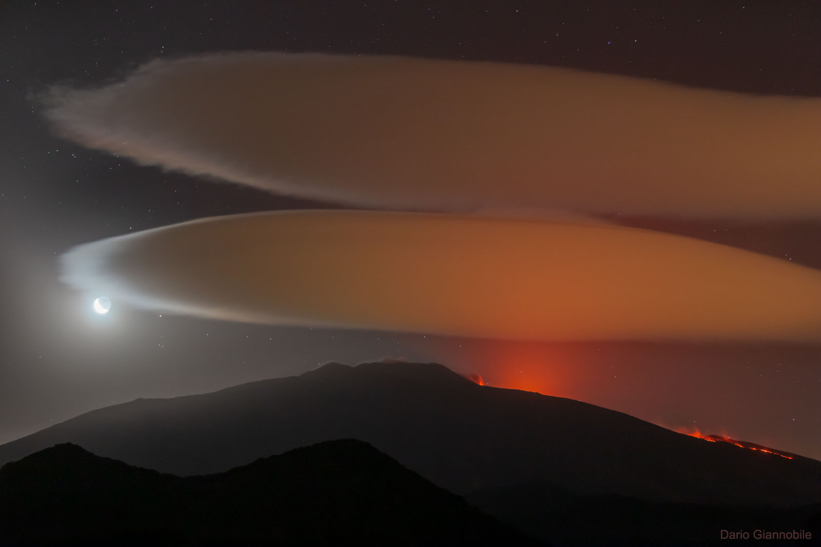 What's happening above that volcano? Although Mount Etna is seen erupting, the clouds are not related to the eruption. They are lenticular clouds formed when moist air is forced upwards near a mountain or volcano.  The surreal scene was captured by chance late last month when the astrophotographer went to Mount Etna, a UNESCO World Heritage Site in Sicily, Italy, to photograph the conjunction between the Moon and the star Aldebaran. The Moon appears in a bright crescent phase, illuminating an edge of the lower lenticular cloud.  Red hot lava flows on the right.  Besides some breathtaking stills, a companion time-lapse video of the scene shows the lenticular clouds forming and wavering as stars trail far in the distance.    Follow APOD in English on: Instagram, Facebook,  Reddit, or Twitter