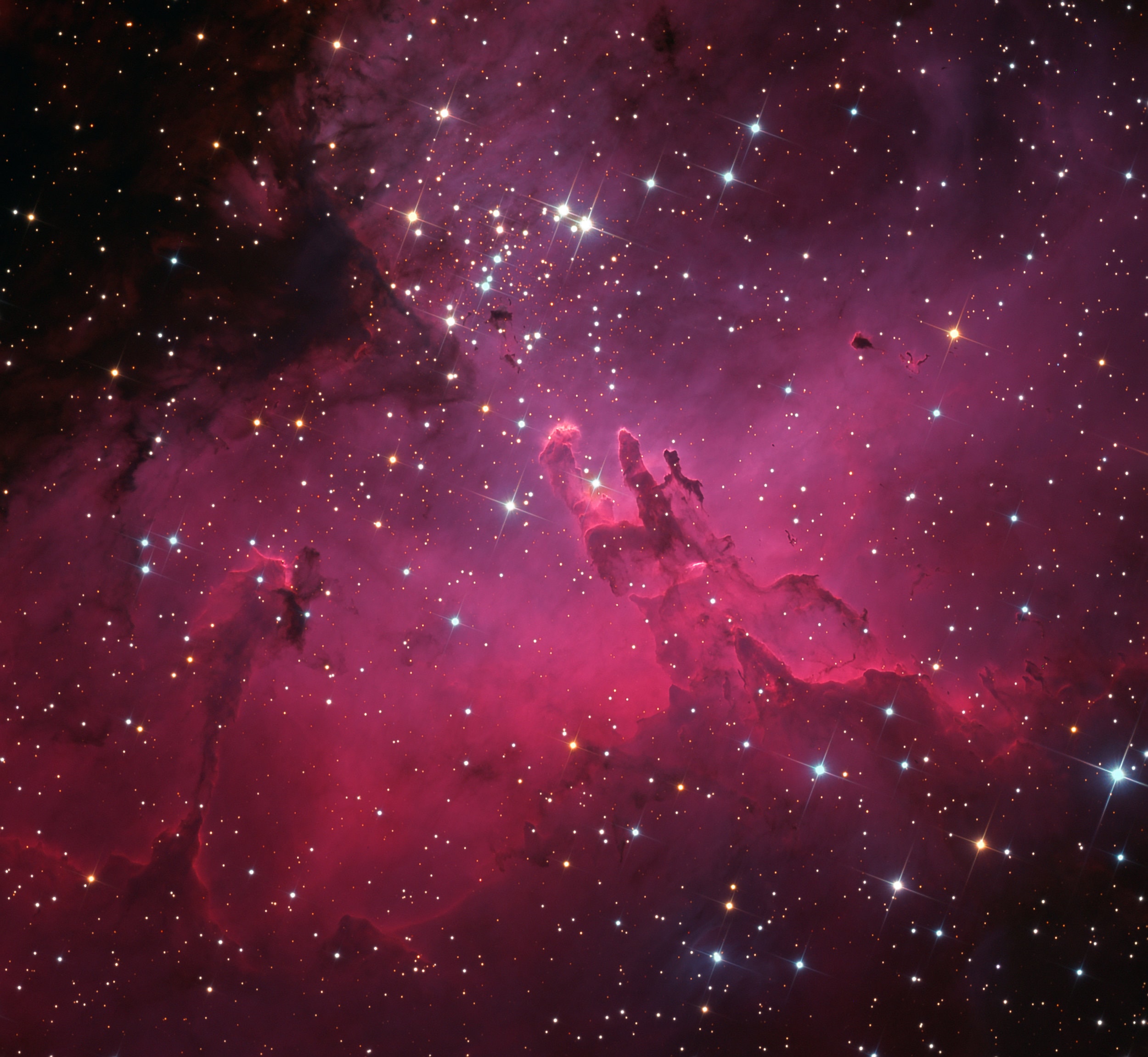 A star cluster around 2 million years young surrounded by natal clouds of dust and glowing gas, M16 is also known as The Eagle Nebula. This beautifully detailed portrait of the region was made with groundbased narrow and broadband image data. It includes cosmic sculptures made famous in Hubble Space Telescope close-ups of the starforming complex. Described as elephant trunks or Pillars of Creation, dense, dusty columns rising near the center are light-years in length but are gravitationally contracting to form stars. Energetic radiation from the cluster stars erodes material near the tips, eventually exposing the embedded new stars. Extending from the ridge of bright emission at lower left is another dusty starforming column known as the Fairy of Eagle Nebula. M16 lies about 7,000 light-years away, an easy target for binoculars or small telescopes in a nebula rich part of the sky toward the split constellation Serpens Cauda (the tail of the snake).