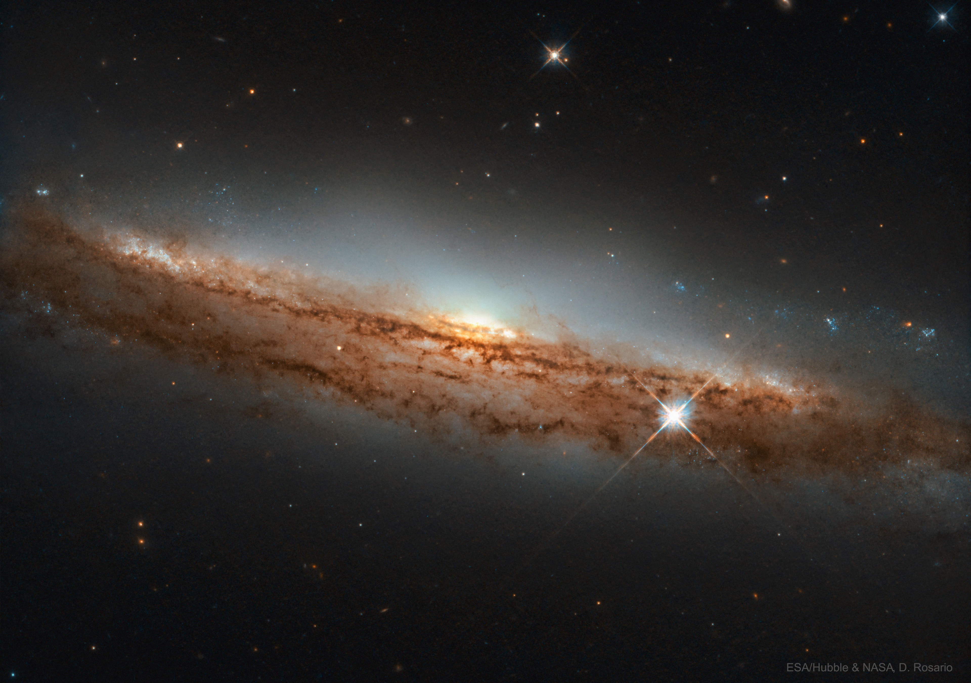 Some spiral galaxies are seen nearly sideways. Most bright stars in spiral galaxies swirl around the center in a disk, and seen from the side, this disk can appear quite thin.  Some spiral galaxies appear even thinner than NGC 3717, which is actually seen tilted just a bit.  Spiral galaxies form disks because the original gas collided with itself and cooled as it fell inward.  Planets may orbit in disks for similar reasons.  The featured image by the Hubble Space Telescope shows a light-colored central bulge composed of older stars beyond filaments of orbiting dark brown dust.  NGC 3717 spans about 100,000 light years and lies about 60 million light years away toward the constellation of the Water Snake (Hydra).   Mercury Crosses the Sun: Some notable images of 2019 transit submitted to APOD