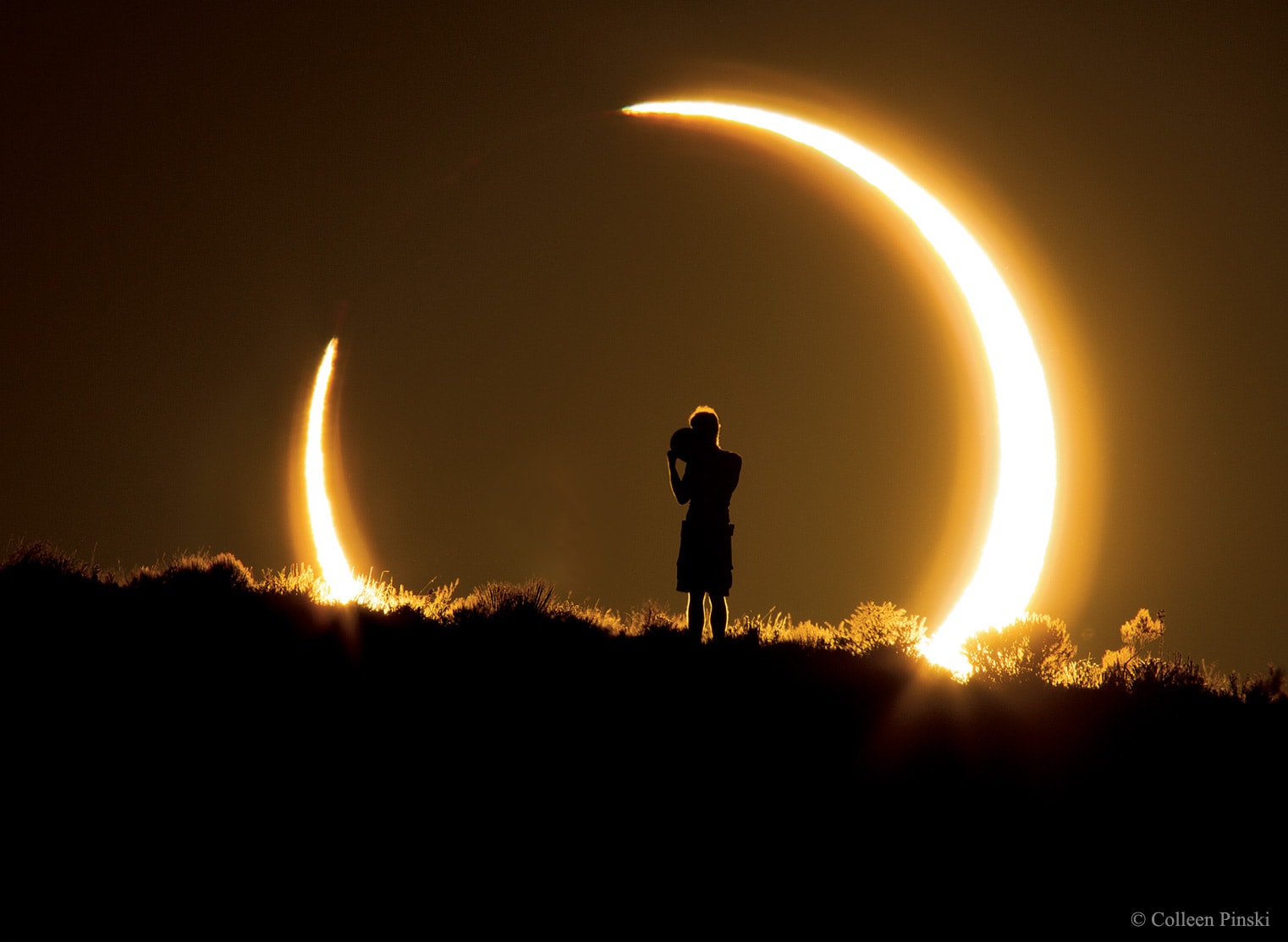 What is this person doing?  In 2012 an annular eclipse of the Sun was visible over a narrow path that crossed the northern Pacific Ocean and several western US states.  In an annular solar eclipse, the Moon is too far from the Earth to block out the entire Sun, leaving the Sun peeking out over the Moon's disk in a ring of fire.  To capture this unusual solar event, an industrious photographer drove from Arizona to New Mexico to find just the right vista. After setting up and just as the eclipsed Sun was setting over a ridge about 0.5 kilometers away, a person unknowingly walked right into the shot. Although grateful for the unexpected human element, the photographer never learned the identity of the silhouetted interloper. It appears likely, though, that the person is holding a circular device that would enable them to get their own view of the eclipse.  The shot was taken at sunset on 2012 May 20 at 7:36 pm local time from a park near Albuquerque, New Mexico, USA. Tomorrow another annular solar eclipse will become visible, this time along a thin path starting in Saudi Arabia and going through southern India, Singapore, and Guam.   However, almost all of Asia with a clear sky will be able to see, tomorrow, at the least, a partial solar eclipse.    Free Download: 2020 APOD Calendar