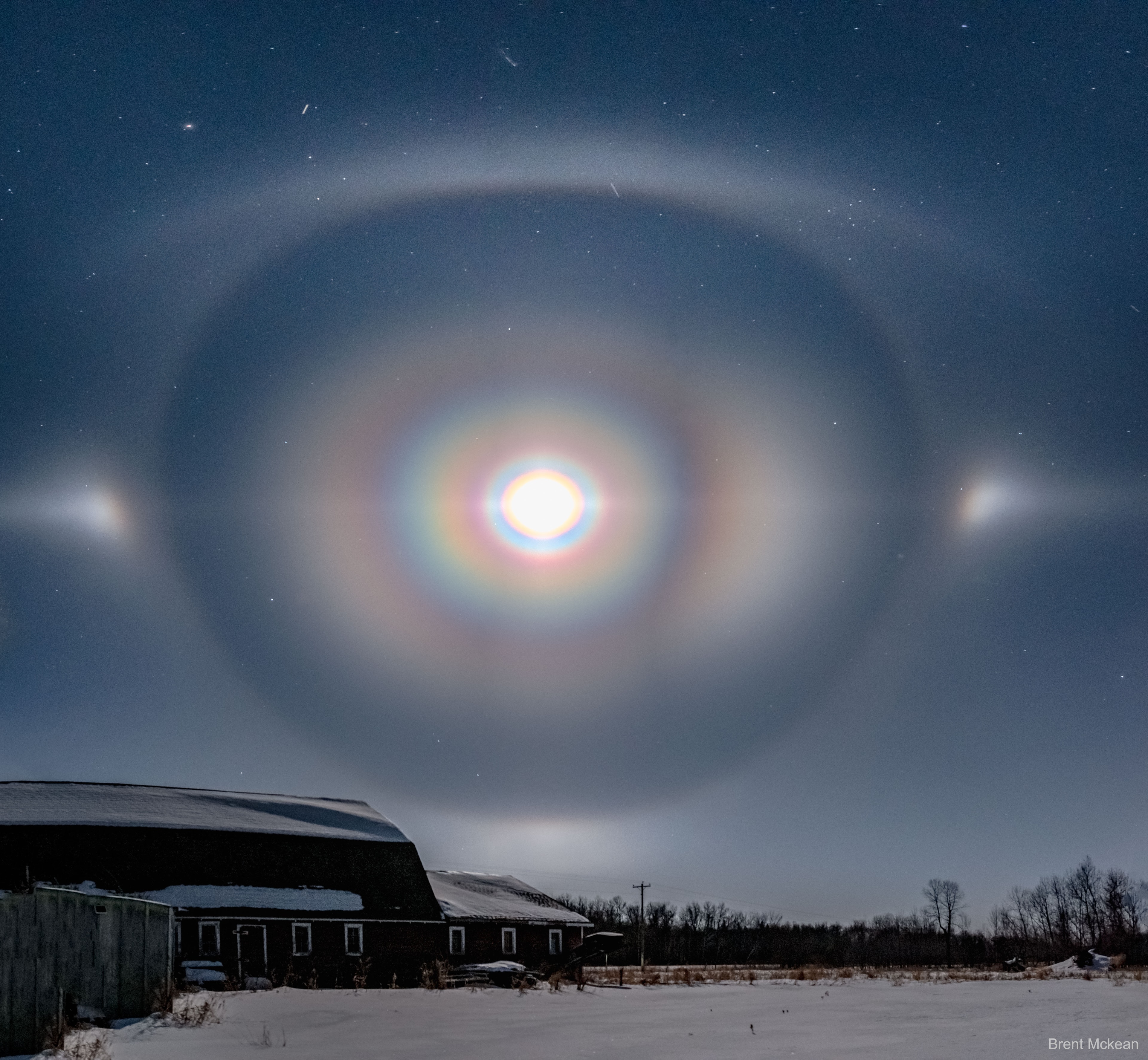 Yes, but could you get to work on time if the Moon looked like this? As the photographer was preparing to drive to work, refraction, reflection, and even diffraction of moonlight from millions of falling ice crystals turned the familiar icon of our Moon into a menagerie of other-worldly halos and arcs. The featured scene was captured with three combined exposures two weeks ago on a cold winter morning in Manitoba, Canada. The colorful rings are a corona caused by quantum diffraction by small drops of water or ice near the direction of the Moon. Outside of that, a 22-degree halo was created by moonlight refracting through six-sided cylindrical ice crystals. To the sides are moon dogs, caused by light refracting through thin, flat, six-sided ice platelets as they flittered toward the ground.  Visible at the top and bottom of the 22-degree halo are upper and lower tangent arcs, created by moonlight refracting through nearly horizontal hexagonal ice cylinders. A few minutes later, from a field just off the road to work, the halo and arcs had disappeared, the sky had returned to normal -- with the exception of a single faint moon dog.