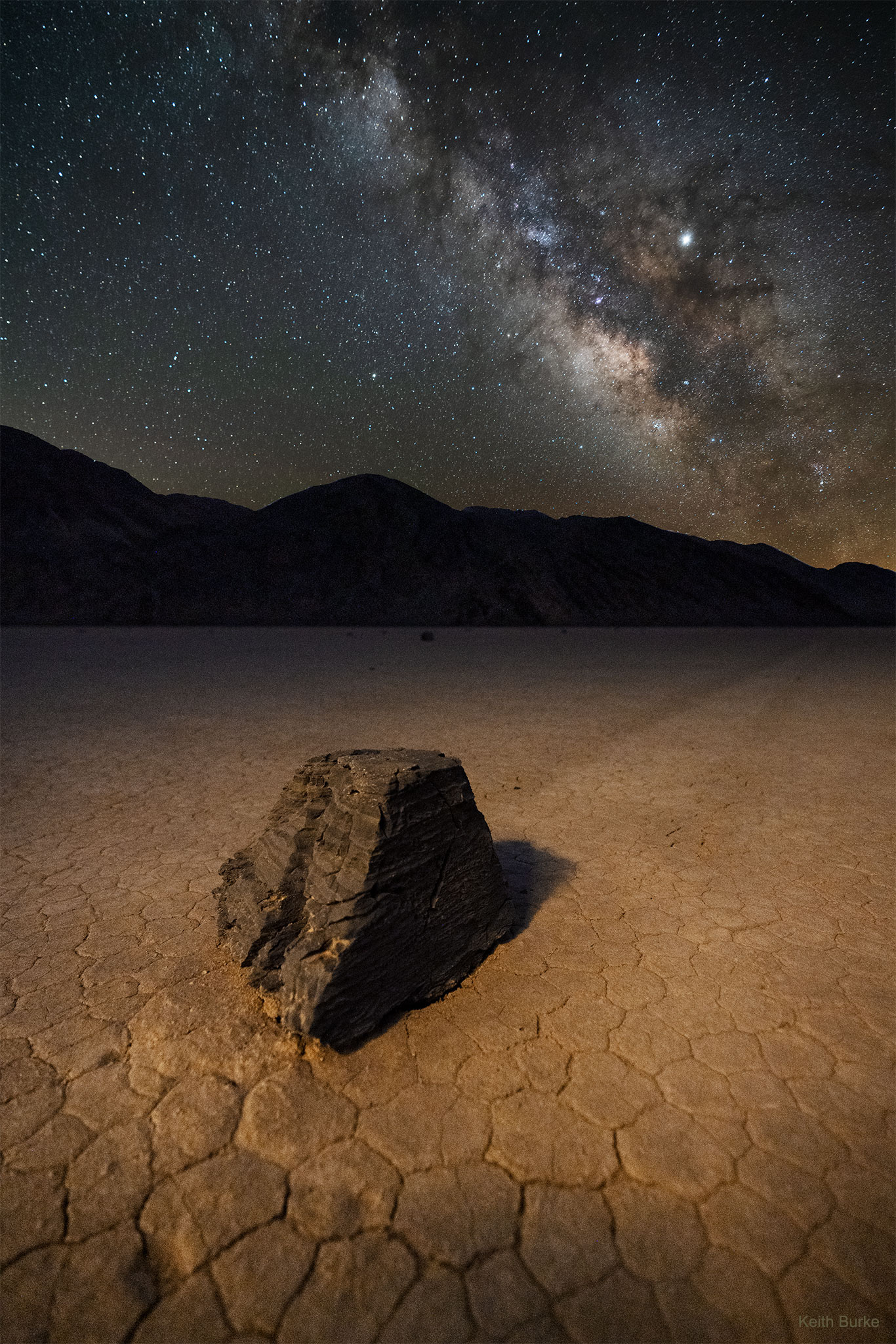 How did this big rock end up on this strange terrain? One of the more unusual places here on Earth occurs inside Death Valley, California, USA.  There a dried lakebed named Racetrack Playa exists that is almost perfectly flat, with the odd exception of some very large stones, one of which is pictured here in April of 2019 beneath a dark, Milky-Way filled sky.  Now the flatness and texture of large playa like Racetrack are fascinating but not scientifically puzzling -- they are caused by mud flowing, drying, and cracking after a heavy rain.  Only recently, however, has a viable scientific hypothesis been given to explain how heavy  sailing stones end up near the middle of such a large flat surface.  Unfortunately, as frequently happens in science, a seemingly surreal problem ends up having a relatively mundane solution.  It turns out that in winter thin floating ice sheets form in a rare ephemeral lake, and light winds push ice sections that then push even heavy rocks across the temporarily flooded playa when sunlight begins to melt the ice.