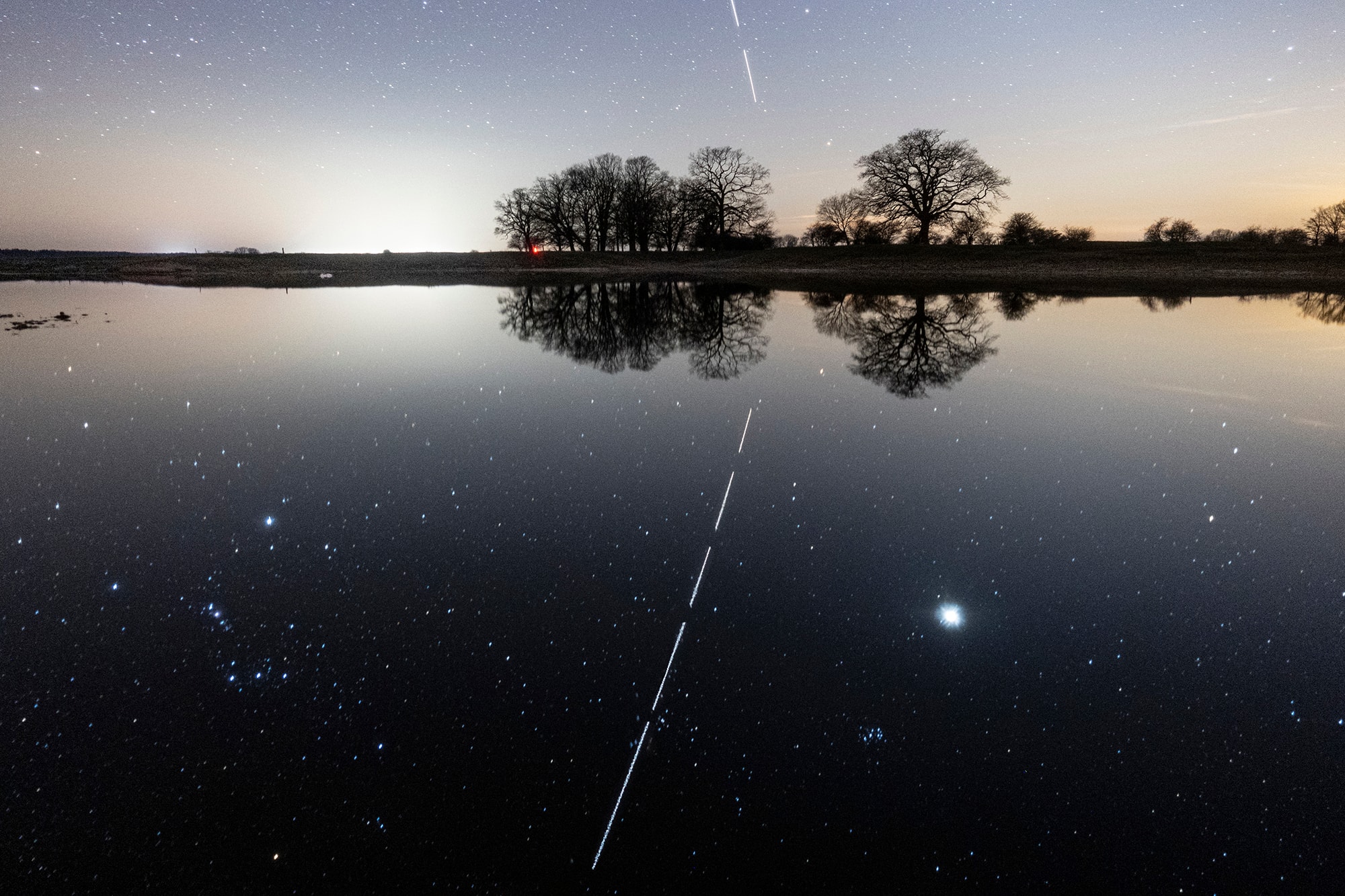 Still bathed in sunlight, the International Space Station arced through the evening sky over lake Wulfsahl-Gusborn in northern Germany, just after sunset on March 25. The familiar constellation of Orion can be seen left of the trail of the orbital station's bright passage. On the right, Venus is the brilliant evening star above the western horizon. With the camera fixed to a tripod, this scene was captured in a series of five exposures. How can you tell? The short time delay between the end of one exposure and the beginning of the next leaves small gaps in the ISS light trail. Look closely and you'll also see that the sky that appears to be above the horizon is actually a reflection though. The final image has been vertically inverted and the night skyscape recorded in the mirror-like waters of the small lake.
