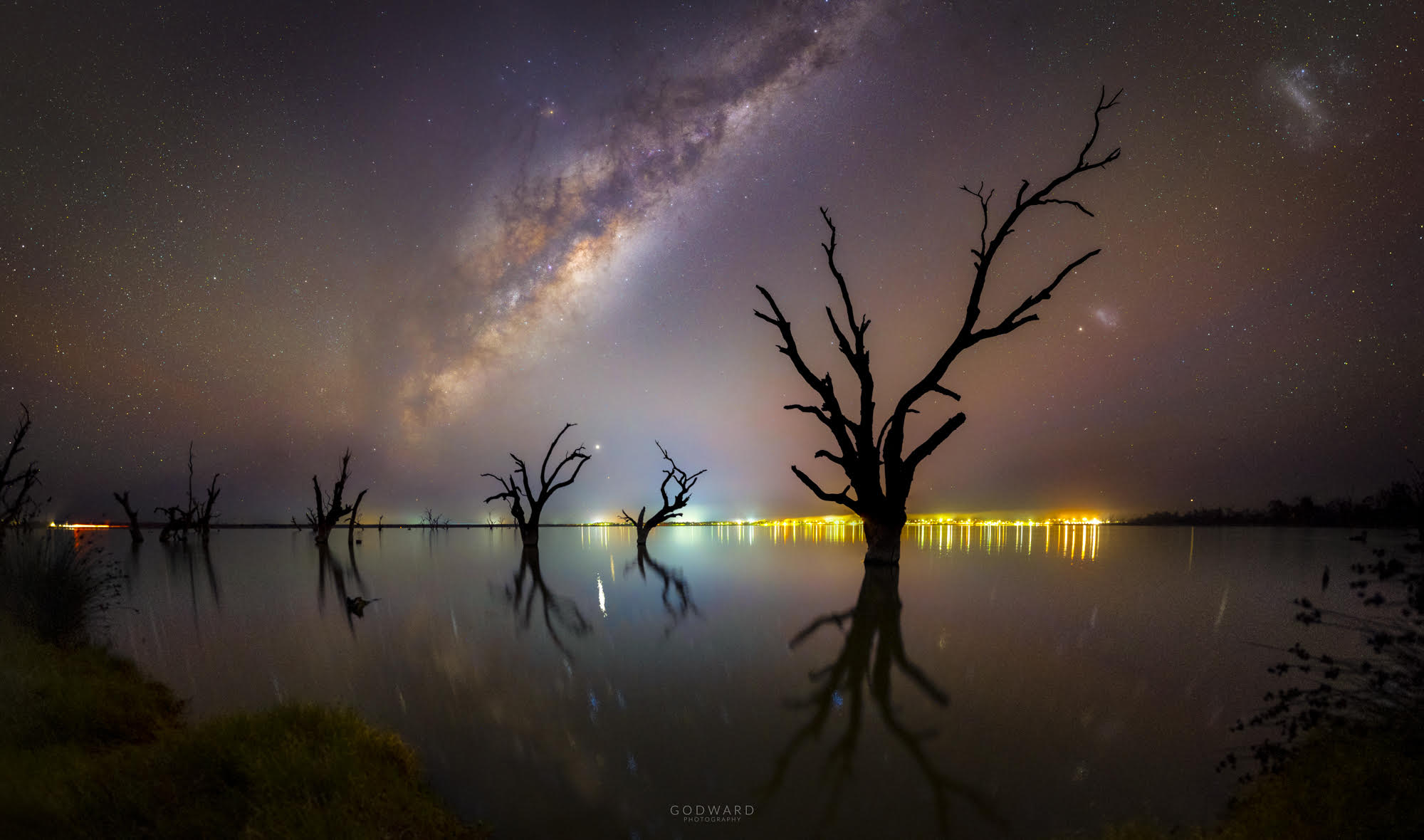 When the lake calmed down, many wonders of the land and sky appeared twice. Perhaps the most dramatic from the dark sky was the central band of our Milky Way Galaxy, visible as a diagonal band. Toward the right were both the Small (SMC) and Large (LMC) Magellanic Clouds, satellite galaxies of our Milky Way. Faint multicolored bands of airglow fanned across the night. Numerous bright stars were visible including Antares, while the bright planet Jupiter appears just above the image center. The featured image is a composite of exposures all taken from the same camera and from the same location within 30 minutes in mid-May from the shore of Lake Bonney Riverland in South Australia. Dead trees that extend from the lake were captured not only in silhouette, but reflection, while lights from the small town of Barmera were visible across the lake. In July, Jupiter and Saturn will rise toward the east just as the Sun sets in the west.