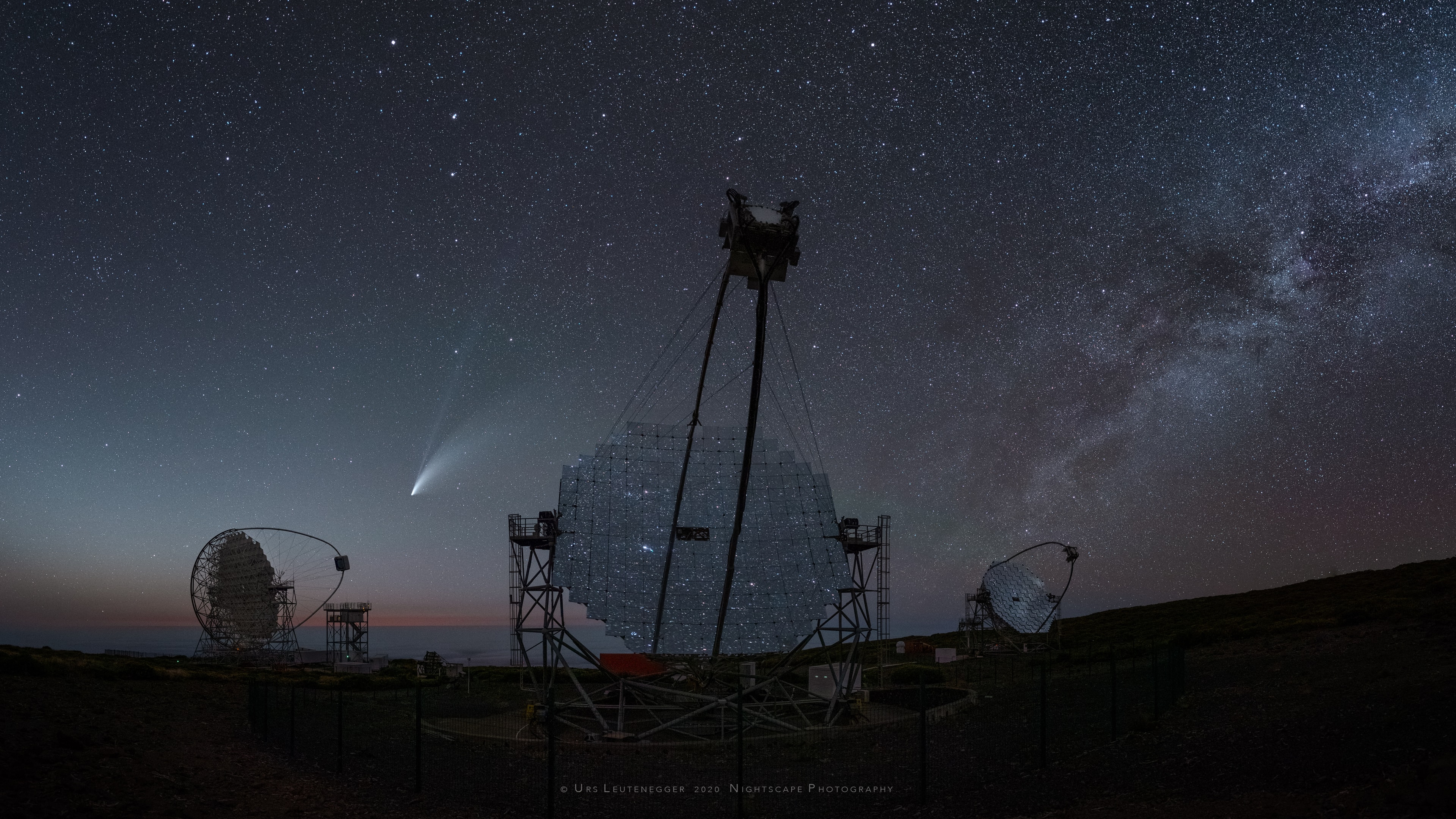 The multi-mirror, 17 meter-diameter MAGIC telescopes reflect this starry night sky from the Roque de los Muchachos European Northern Observatory on the Canary Island of La Palma. MAGIC stands for Major Atmospheric Gamma Imaging Cherenkov and the telescopes can see the brief flashes of optical light produced in particle air showers as high-energy gamma rays impact the Earth's upper atmosphere. On July 20, two of the three telescopes in view were looking for gamma rays from the center of our Milky Way galaxy. In reflection they show the bright stars of Sagittarius and Scorpius near the galactic center to the southeast. Beyond the segmented-mirror arrays, above the northwest horizon and below the Big Dipper is Comet NEOWISE. NEOWISE stands for Near Earth Object Wide-field Infrared Survey Explorer. That's the Earth-orbiting satellite used to discover the comet designated C/2020 F3, but you knew that.  Comet NEOWISE Images:  July  23 || 22 || 21 || 20 || 19  || 18   || 17   || 16   || 15  || 14  || 13  || 12  || 11  || 10 & earlier