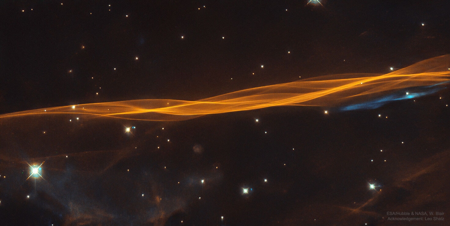 What lies at the edge of an expanding supernova?  Subtle and delicate in appearance, these ribbons of shocked interstellar gas are part of a blast wave at the expanding edge of a violent stellar explosion that would have been easily visible to humans during the late stone age, about 20,000 years ago.  The featured image was recorded by the Hubble Space Telescope and is a closeup of the outer edge of a supernova remnant known as the Cygnus Loop or Veil Nebula.  The filamentary shock front is moving toward the top of the frame at about 170 kilometers per second, while glowing in light emitted by atoms of excited hydrogen gas.  The distances to stars thought to be interacting with the Cygnus Loop have recently been found by the Gaia mission to be about 2400 light years distant.  The whole Cygnus Loop spans six full Moons across the sky, corresponding to about 130 light years, and parts can be seen with a small telescope toward the constellation of the Swan (Cygnus).