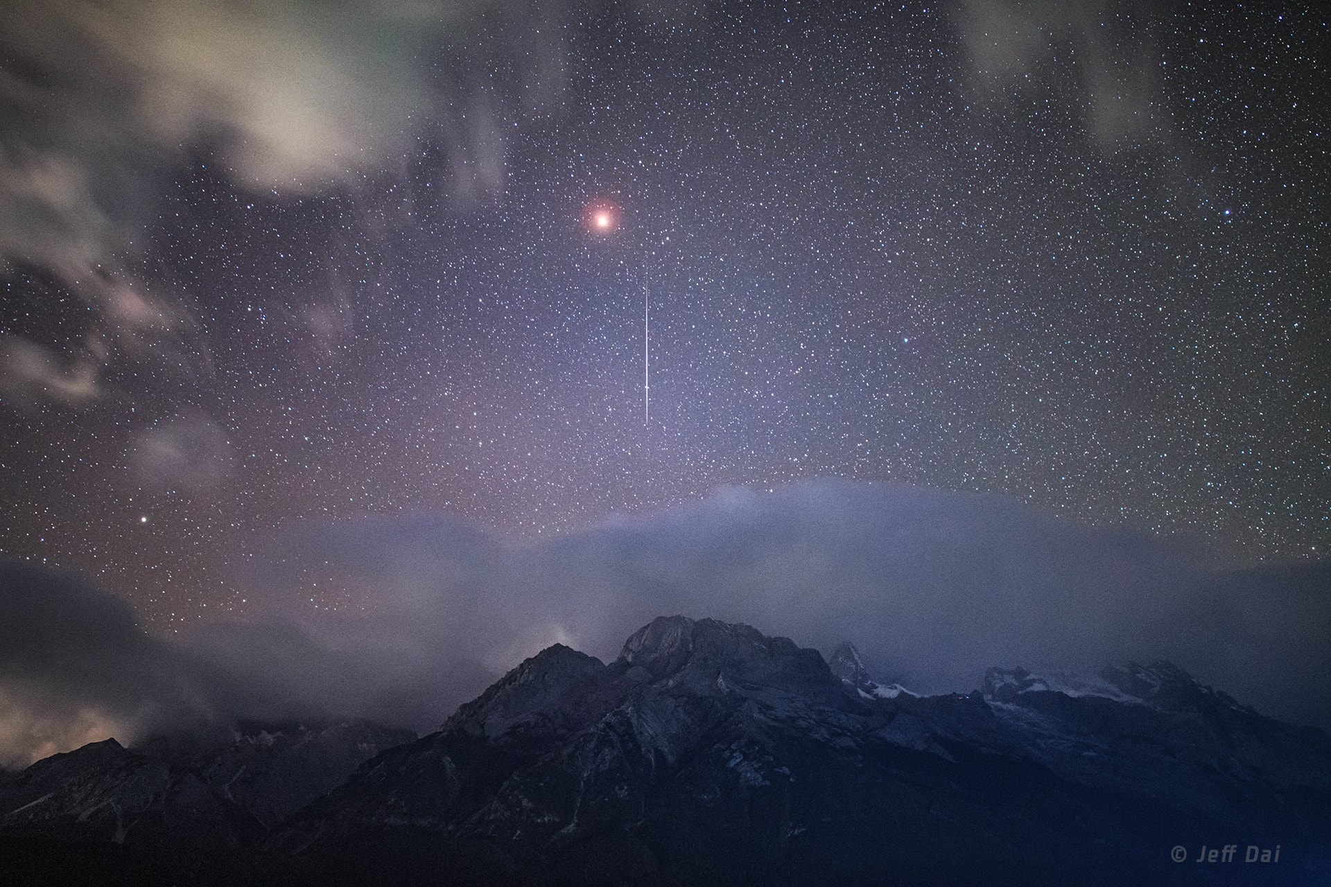 A brilliant yellowish celestial beacon, Mars still dazzles in the night. Peering between clouds the wandering planet was briefly joined by the flash of a meteor in this moonless dark sky on November 18. The single exposure was taken as the Earth swept up dust from periodic comet Tempel-Tuttle during the annual Leonid Meteor Shower. The view of a rugged western horizon looks along the Yulong mountain range in Yunnan province, southwestern China. Yulong (Jade Dragon) Snow Mountain lies below the clouds and beyond the end of the meteor streak.