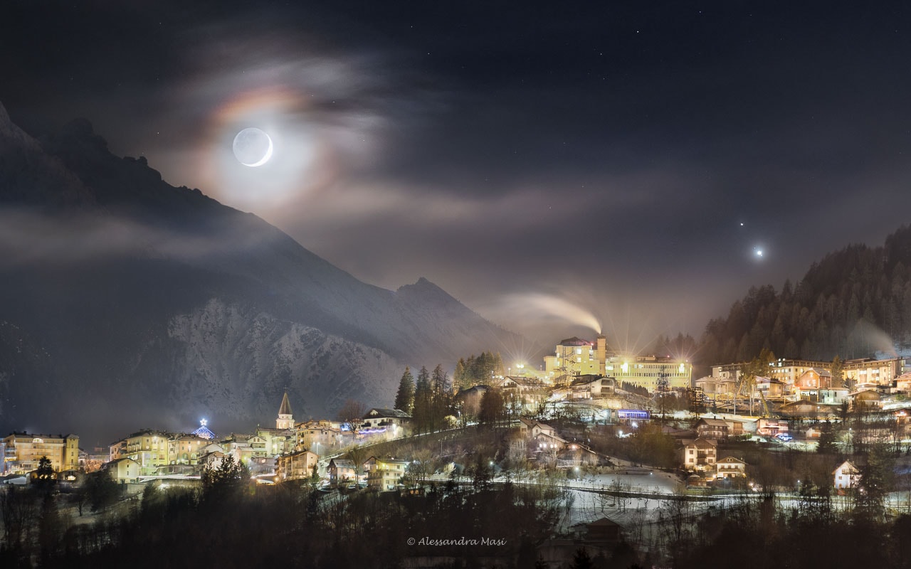 Why does a cloudy moon sometimes appear colorful? The effect, called a lunar corona, is created by the quantum mechanical diffraction of light around individual, similarly-sized water droplets in an intervening but mostly-transparent cloud. Since light of different colors has different wavelengths, each color diffracts differently. Lunar Coronae are one of the few  quantum mechanical color effects that can be easily seen with the unaided eye.  Solar coronae are also sometimes evident.  The featured composite image was captured a few days before the close Great Conjunction between Saturn and Jupiter last month. In the foreground, the Italian village of Pieve di Cadore is visible in front of the Sfornioi Mountains.    New: APOD is now available in Taiwanese from National Central University