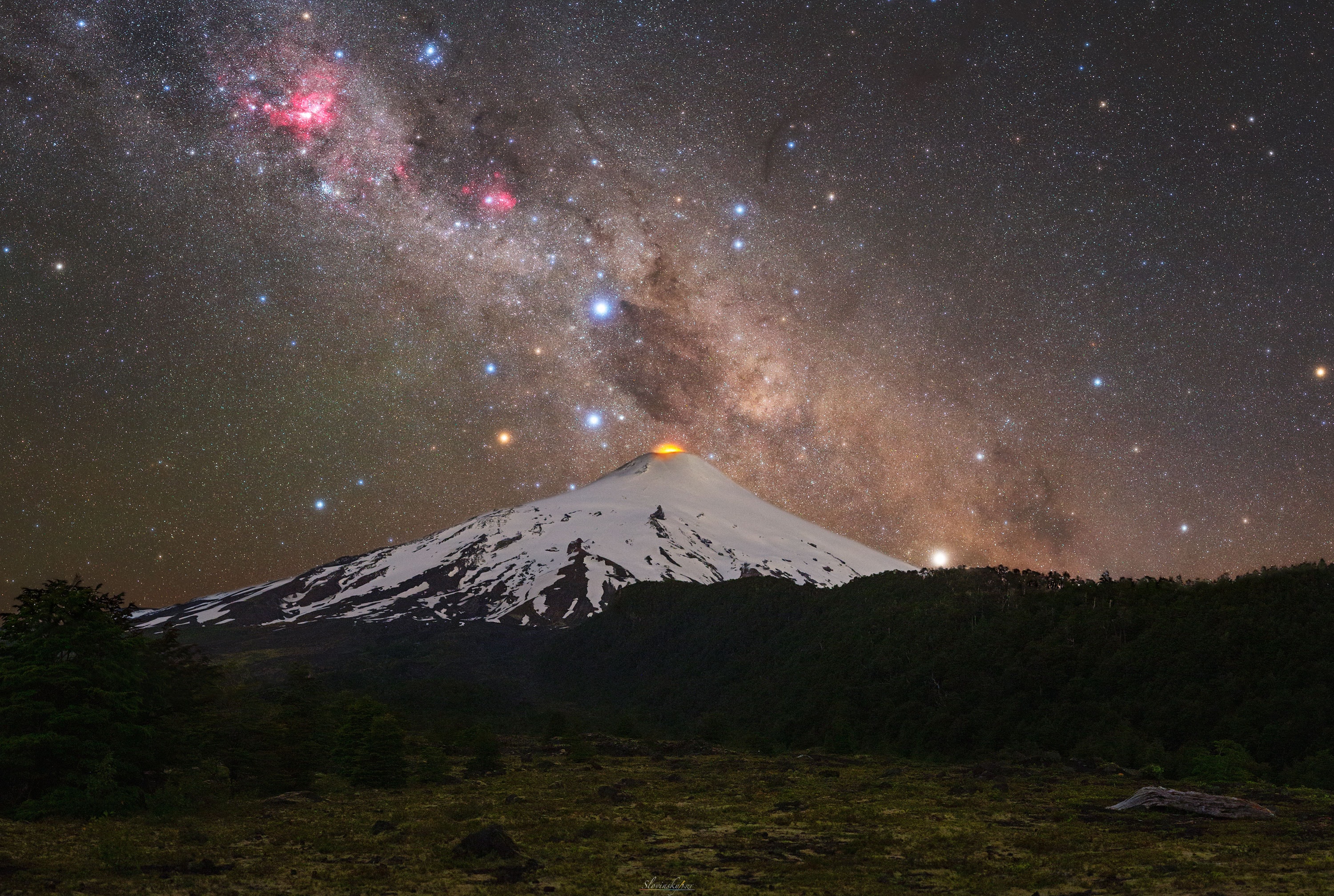 Have you ever seen the Southern Cross? This famous four-star icon is best seen from Earth's Southern Hemisphere. The featured image was taken last month in Chile and captures the Southern Cross just to the left of erupting Villarrica, one of the most active volcanos in our Solar System.  Connecting the reddest Southern Cross star Gacrux through the brightest star  Acrux points near the most southern location in the sky: the South Celestial Pole (SCP), around which all southern stars appear to spin as the Earth turns. In modern times, no bright star resides near the SCP, unlike in the north where bright Polaris now appears near the NCP.  Extending the Gacrux - Acrux line still further (from about four to about seven times their angular separation) leads near the Small Magellanic Cloud, a bright satellite galaxy of our Milky Way Galaxy.  The Southern Cross asterism dominates the Crux constellation, a deeper array of stars that includes four Cepheid variable stars visible to the unaided eye. Just above the volcano in the image, and looking like a dark plume, is the Coalsack Nebula, while the large red star-forming Carina Nebula is visible on the upper left.   Portal Universe: Random APOD Generator