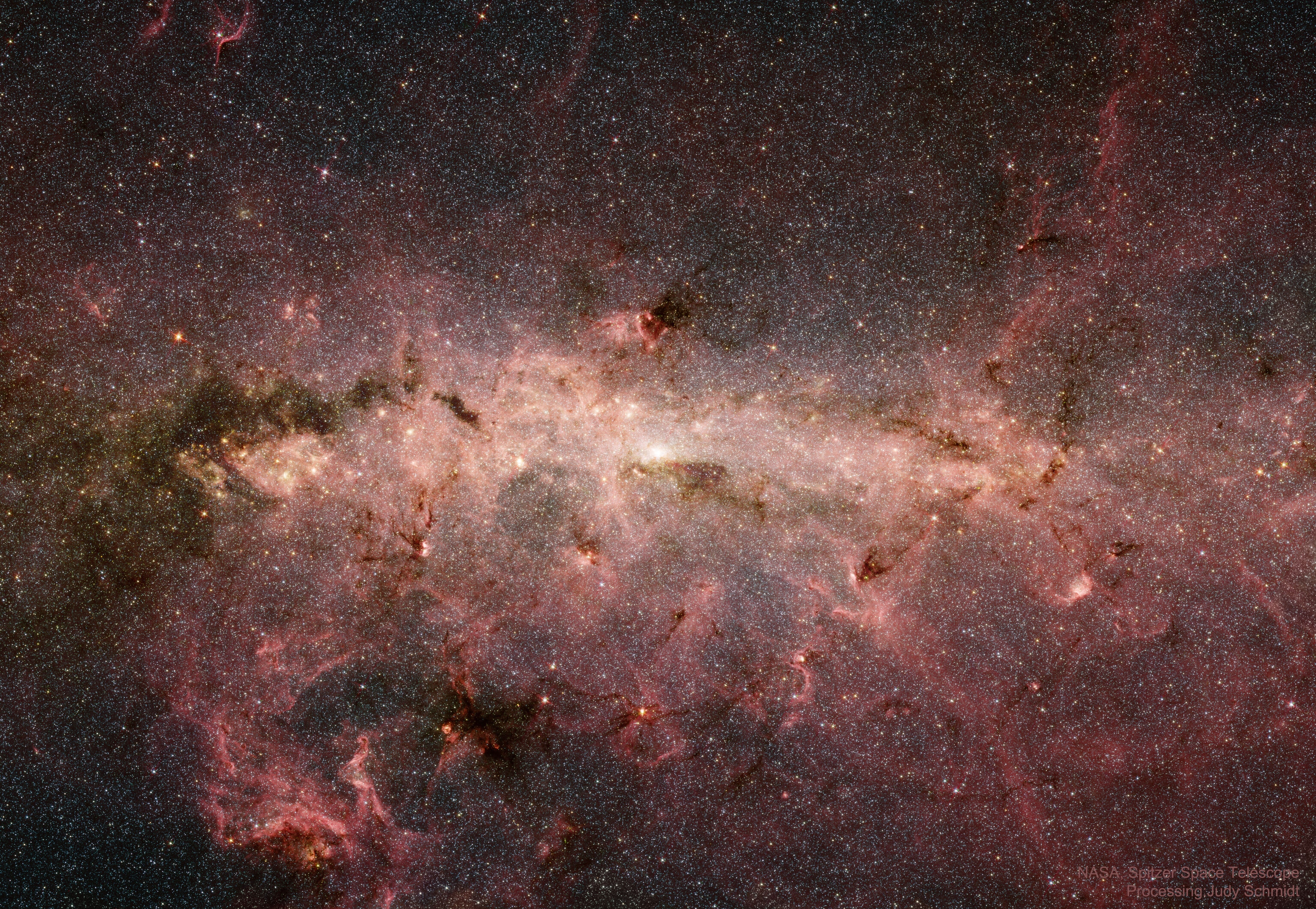 What does the center of our galaxy look like?  In visible light, the Milky Way's center is hidden by clouds of obscuring dust and gas. But in this stunning vista, the Spitzer Space Telescope's infrared cameras, penetrate much of the dust revealing the stars of the crowded galactic center region. A mosaic of many smaller snapshots, the detailed, false-color image shows older, cool stars in bluish hues. Red and brown glowing dust clouds are associated with young, hot stars in stellar nurseries. The very center of the Milky Way has recently been found capable of forming newborn stars. The galactic center lies some 26,700 light-years away, toward the constellation Sagittarius. At that distance, this picture spans about 900 light-years.