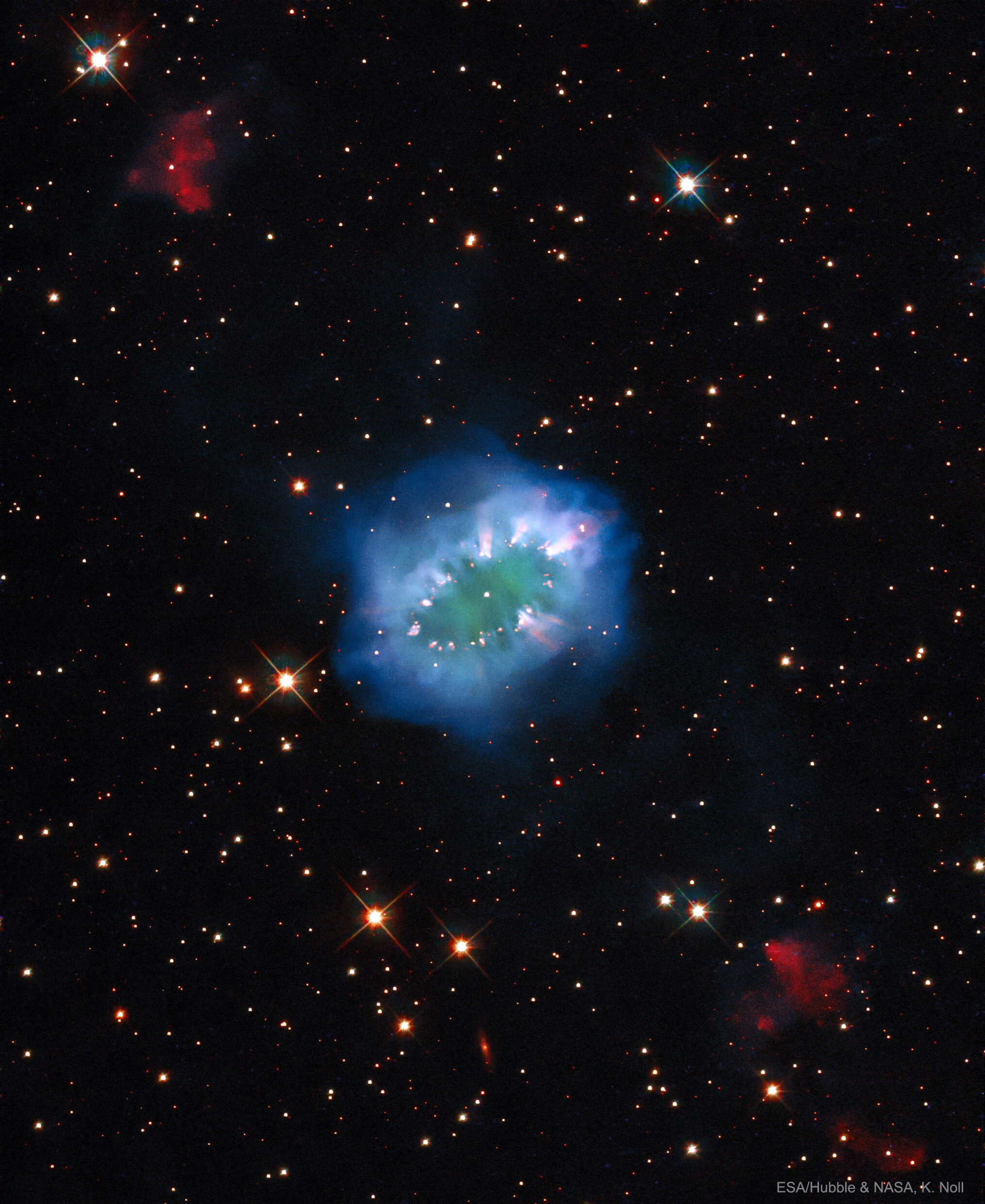 What celestial body wears the Necklace Nebula? First, analyses indicate that the Necklace is a planetary nebula, a gas cloud emitted by a star toward the end of its life. Also, what appears to be diamonds in the Necklace are actually bright knots of glowing gas.  In the center of the Necklace Nebula are likely two stars orbiting so close together that they share a common atmosphere and appear as one in the featured image by the Hubble Space Telescope.  The red-glowing gas clouds on the upper left and lower right are the results of jets from the center.  Exactly when and how the bright jets formed remains a topic of research.  The Necklace Nebula is only about 5,000 years old, spans about 5 light years, and can best be found with a large telescope toward the direction of the constellation of the Arrow (Sagitta).