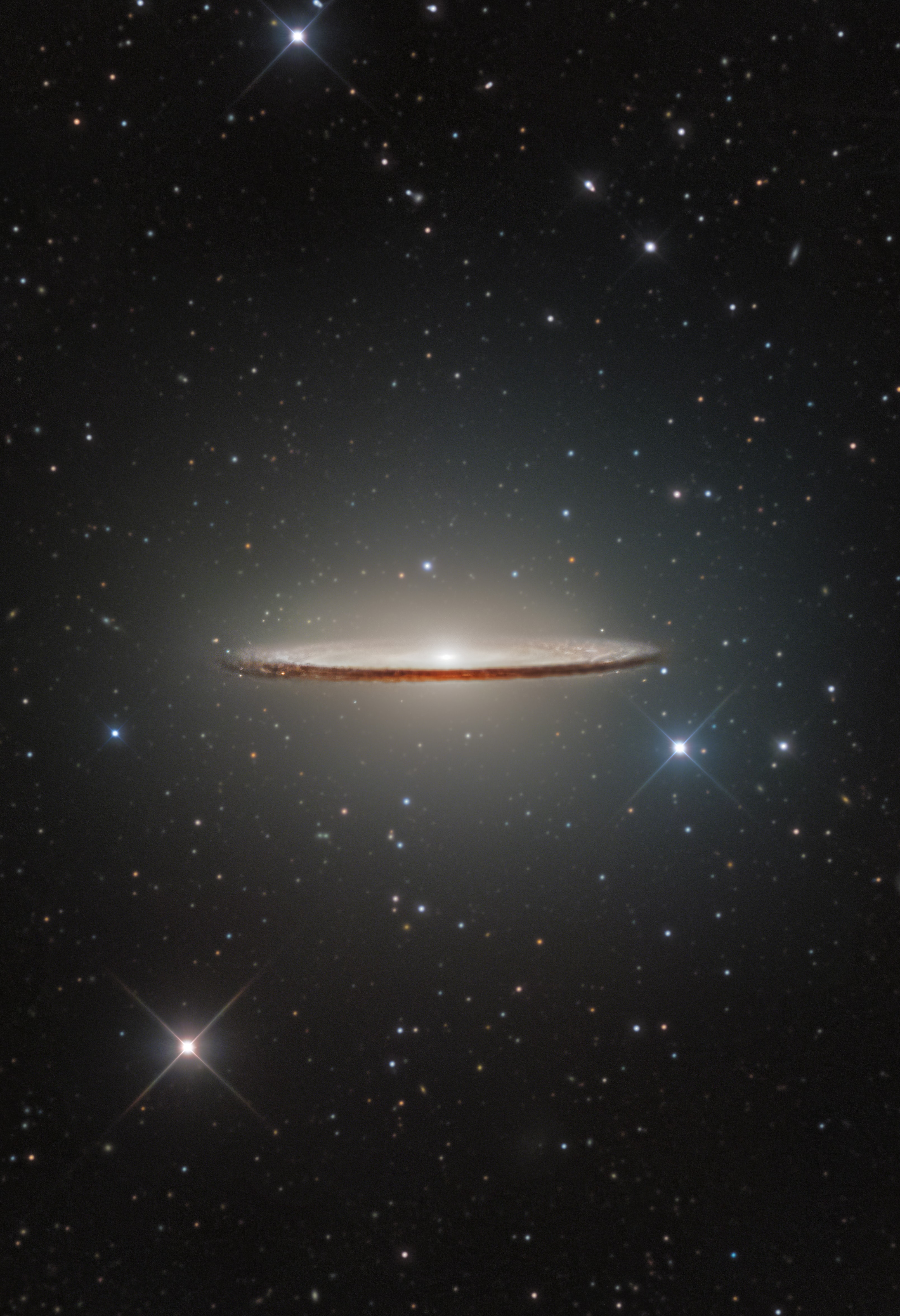 A gorgeous spiral galaxy, M104 is famous for its nearly edge-on profile featuring a broad ring of obscuring dust lanes. Seen in silhouette against an extensive central bulge of stars, the swath of cosmic dust lends a broad brimmed hat-like appearance to the galaxy suggesting a more popular moniker, the Sombrero Galaxy. This sharp optical view of the well-known galaxy made from ground-based image data was processed to preserve details often lost in overwhelming glare of M104's bright central bulge. Also known as NGC 4594, the Sombrero galaxy can be seen across the spectrum, and is host to a central supermassive black hole. About 50,000 light-years across and 28 million light-years away, M104 is one of the largest galaxies at the southern edge of the Virgo Galaxy Cluster. Still the colorful spiky foreground stars in this field of view lie well within our own Milky Way galaxy.