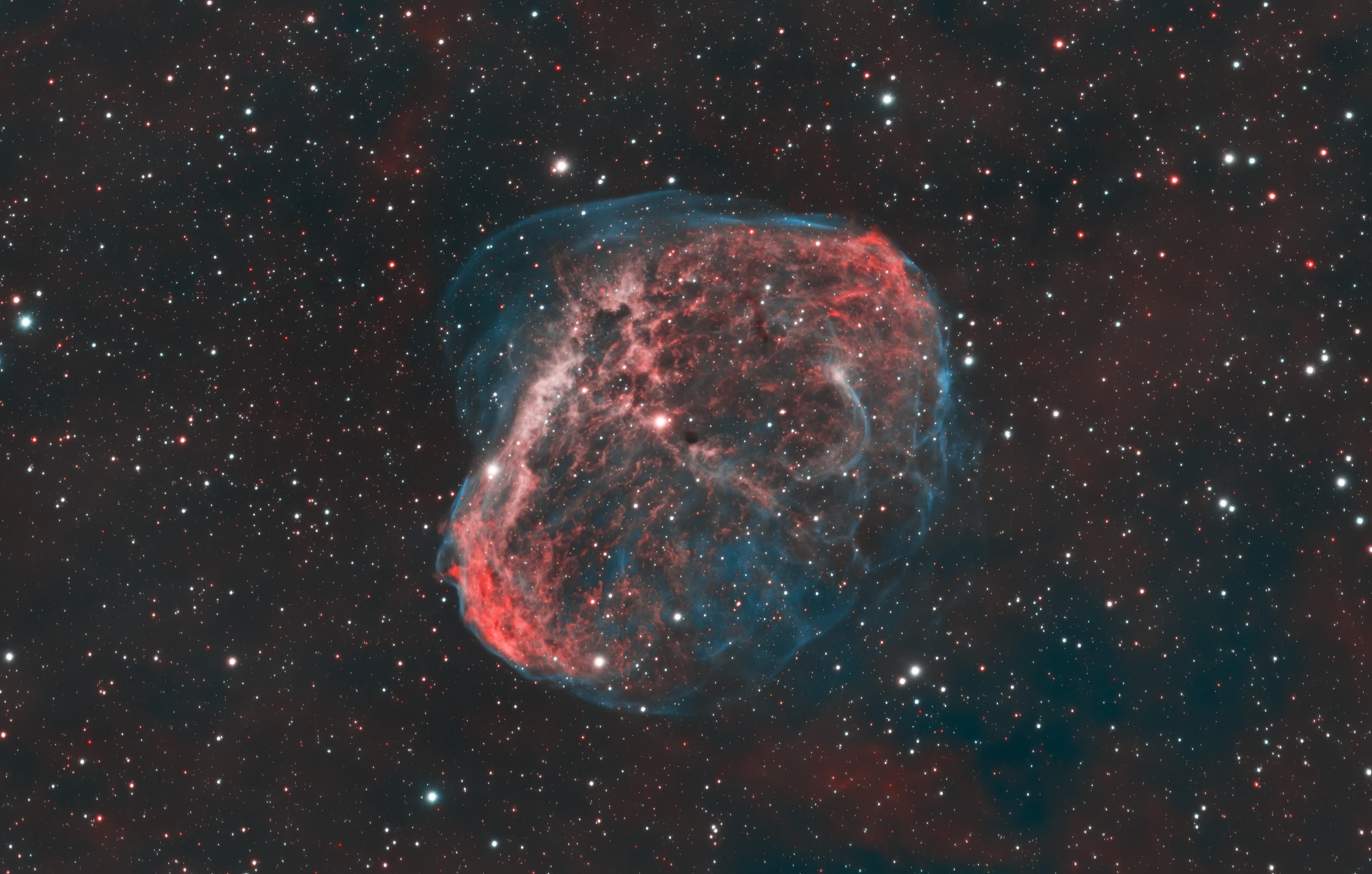 NGC 6888, also known as the Crescent Nebula, is a about 25 light-years across blown by winds from its central, bright, massive star. A triumvirate of astroimagers ( Joe, Glenn, Russell) created this sharp portrait of the cosmic bubble. Their telescopic collaboration collected over 30 hours of narrow band image data isolating light from hydrogen and oxygen atoms. The oxygen atoms produce the blue-green hue that seems to enshroud the detailed folds and filaments. Visible within the nebula, NGC 6888's central star is classified as a Wolf-Rayet star (WR 136). The star is shedding its outer envelope in a strong stellar wind, ejecting the equivalent of the Sun's mass every 10,000 years.  The nebula's complex structures are likely the result of this strong wind interacting with material ejected in an earlier phase. Burning fuel at a prodigious rate and near the end of its stellar life this star should ultimately go out with a bang in a spectacular supernova explosion. Found in the nebula rich constellation Cygnus, NGC 6888 is about 5,000 light-years away.