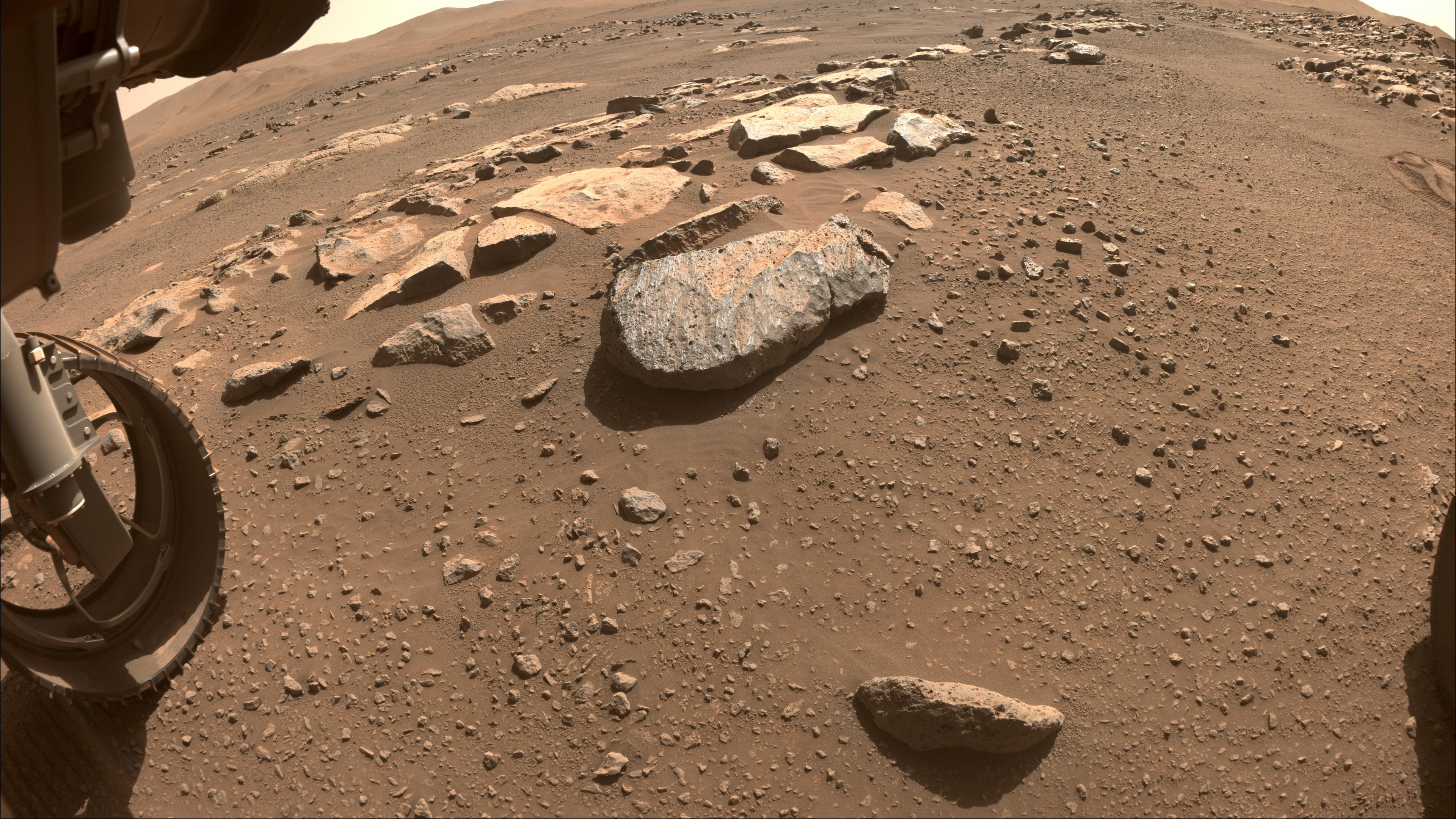 Taken on mission sol 180 (August 22) this sharp image from a Hazard Camera on the Perseverance rover looks out across a rock strewn floor of Jezero crater on Mars. At 52.5 centimeters (21 inches) in diameter, one of the rover's steerable front wheels is at lower left in the frame. Near center is a large rock nicknamed Rochette. Mission planners don't want to avoid Rochette though. Instead Perseverance will be instructed to reach out with its 2 meter long robotic arm and abrade the rock's surface, to determine whether it has a consistency suitable for obtaining a sample, slightly thicker than a pencil, using the rover's coring bit. Samples collected by Perseverance would be returned to Earth by a future Mars mission.