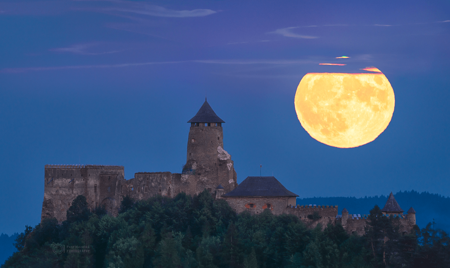 On July 13 this well-planned telephoto view recorded a Full Moon rising over Lubovna Castle in eastern Slovakia. The photographer was about 3 kilometers from the castle walls and about 357,000 kilometers from this Full Moon near perigee, the closest point in its elliptical orbit. Known to some as supermoons, full moons near perigee are a little brighter and larger in planet Earth's sky when compared to full moons that occur near the average lunar distance of around 384,000 kilometers. Of course any Full Moon near the horizon can show the effects of refraction over a long sight-line through dense clear atmosphere. In this image, atmospheric refraction creates the slight green flash framed by thin clouds near the top, with a ragged red rim along the bottom edge of July's perigee Full Moon.