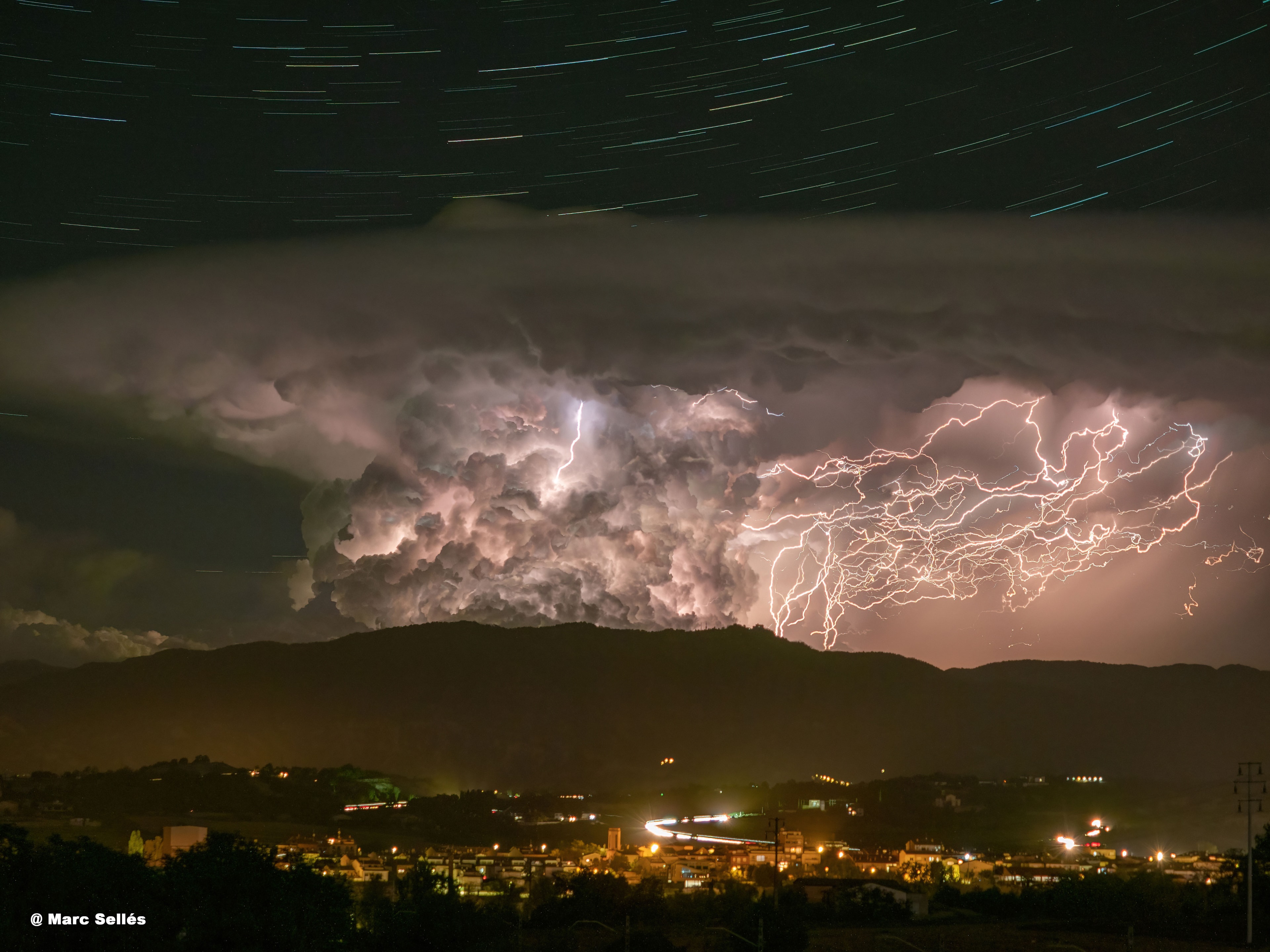 The beauty in this image comes in layers. On the bottom layer is the picturesque village of Manlleu in Barcelona, Spain.  The six-minute exposure makes car lights into streaks. The next layer is a mountain -- Serra de Bellmunt -- of Europe's famous Pyrenees. Next up is a tremendous lightning storm emanating from a classically-shaped anvil cloud. The long exposure allowed for the capture of many intricate lightning bolts.  Finally, at the top and furthest in the distance are stars.  Here, the multi-minute exposure made stars into trails.  The trailing effect is caused by the rotation of the Earth, and the curvature of the trails indicates their distance from the north spin pole of the Earth above. Taken after sunset in early June, the lightning storm soon moved off.  The stars, though, will continue to circle the pole for as long as the Earth spins -- surely billions of years into the future.