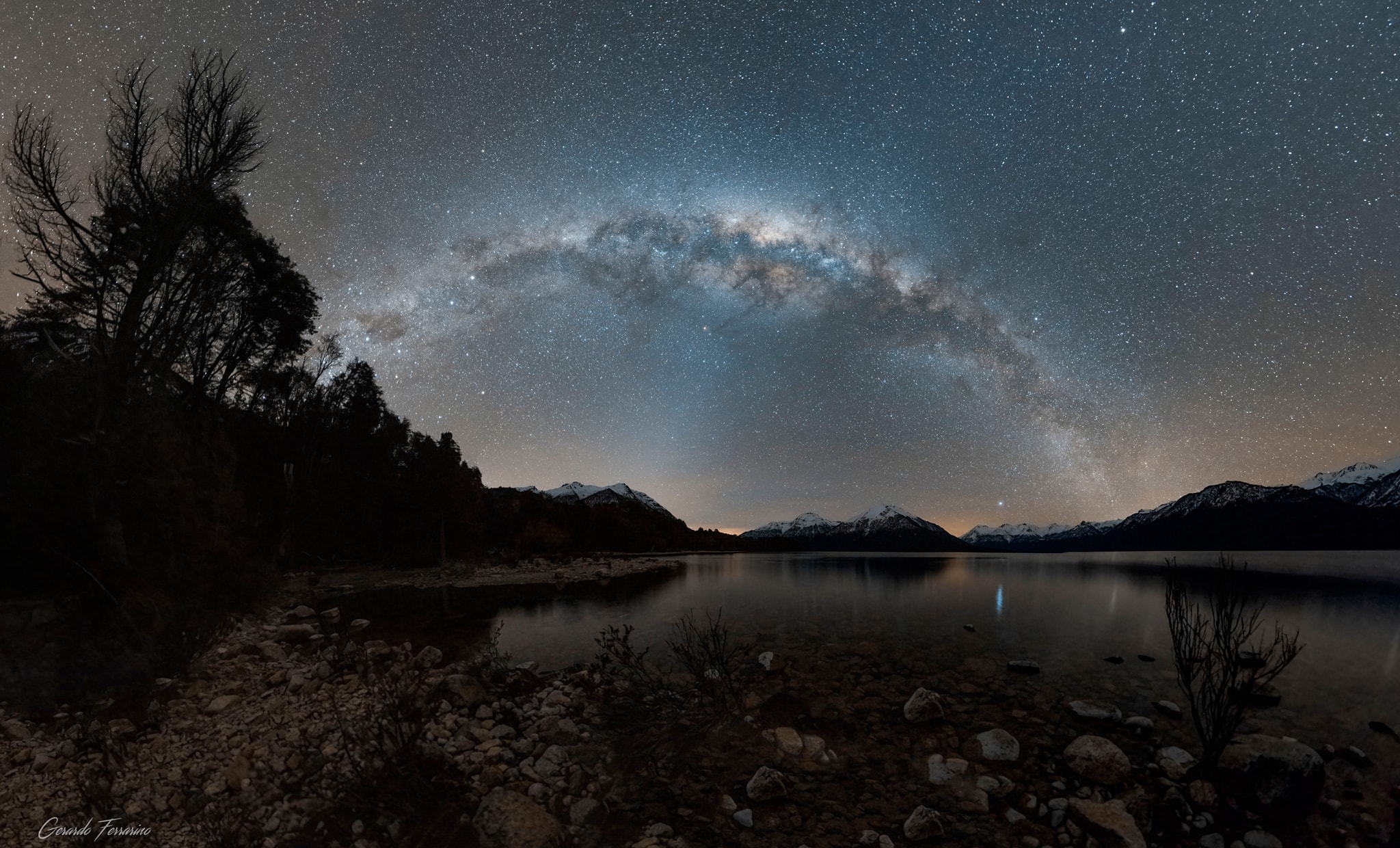This 180 degree panoramic night skyscape captures our Milky Way Galaxy as it arcs above the horizon on a winter's night in August. Near midnight, the galactic center is close to the zenith with the clear waters of Lake Traful, Neuquen, Argentina, South America, planet Earth below. Zodiacal light, dust reflected sunlight along the Solar System's ecliptic plane, is also visible in the region's very dark night sky. The faint band of light reaches up from the distant snowy peaks toward the galaxy's center. Follow the arc of the Milky Way to the left to find the southern hemisphere stellar beacons Alpha and Beta Centauri. Close to the horizon bright star Vega is reflected in the calm mountain lake.