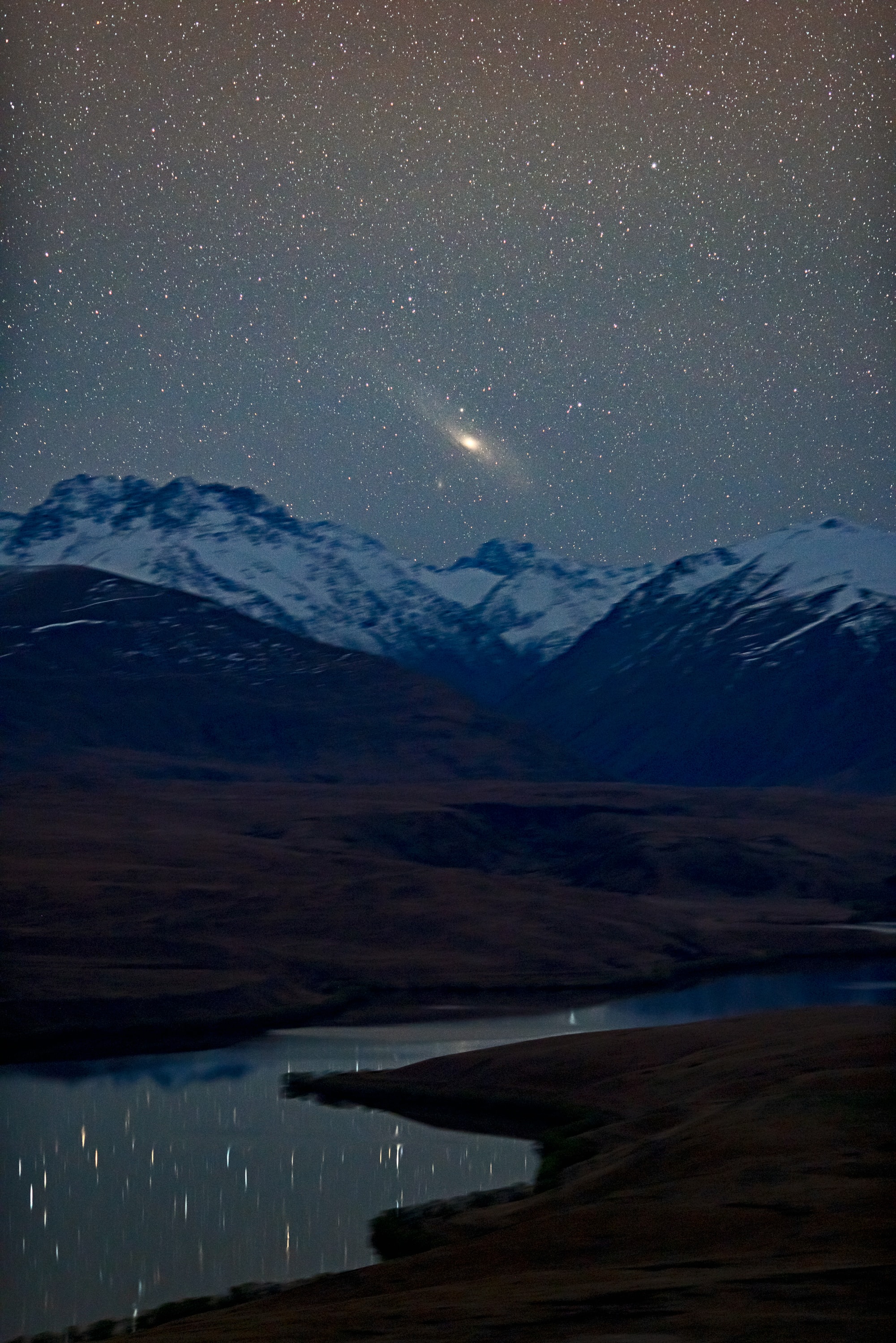 Looking north from southern New Zealand, the Andromeda Galaxy never gets more than about five degrees above the horizon. As spring comes to the southern hemisphere, in late September Andromeda is highest in the sky around midnight though. In a single 30 second exposure this telephoto image tracked the stars to capture the closest large spiral galaxy from Mount John Observatory as it climbed just over the rugged peaks of the south island's Southern Alps. In the foreground, stars are reflected in the still waters of Lake Alexandrina. Also known as M31, the Andromeda Galaxy is one of the brightest objects in the Messier catalog, usually visible to the unaided eye as a small, faint, fuzzy patch. But this clear, dark sky and long exposure reveal the galaxy's greater extent in planet Earth's night, spanning nearly 6 full moons.