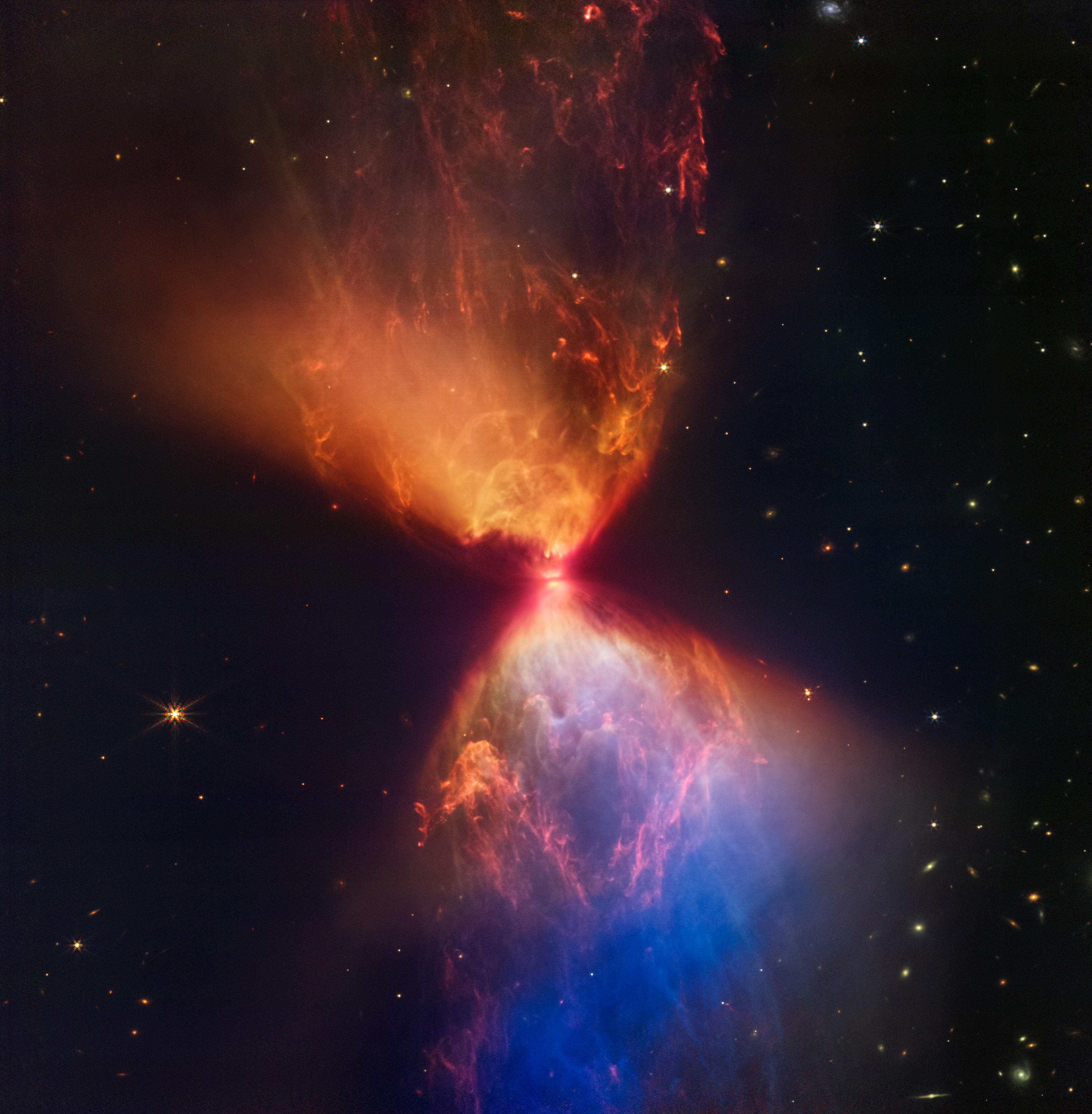 The protostar within dark cloud L1527 is a mere 100,000 years old, still embedded in the cloud of gas and dust that feeds its growth. In this NIRCam image from the James Webb Space Telescope, the dark band at the neck of the infrared nebula is a thick disk that surrounds the young stellar object.  Viewed nearly edge-on and a little larger than our Solar System, the disk ultimately supplies material to the protostar while hiding it from Webb's direct infrared view. The nebula itself is seen in stunning detail though. Illuminated by infrared light from the protostar, the hourglass-shaped nebula's cavities are created as material ejected in the star-forming process plows through the surrounding medium. As the protostar gains mass it will eventually become a full-fledged star, collapsing and igniting nuclear fusion in its core. A likely analog to our own Sun and Solar System in their early infancy, the protostar within dark cloud L1527 lies some 460 light-years distant in the Taurus star-forming region. Webb's NIRCam image spans about 0.3 light-years.