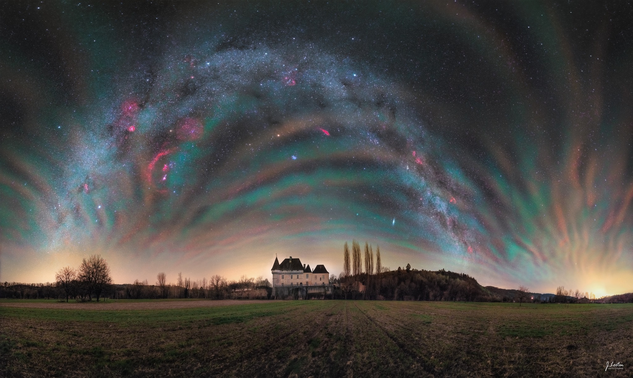 This unusual sky was both familiar and unfamiliar. The photographer's mission was to capture the arch of the familiar central band of our Milky Way Galaxy over a picturesque medieval manor.  The surprise was that on this January evening, the foreground sky was found glowing in a beautiful but unfamiliar manner. The striped bands are called airglow and they result from air high in Earth's atmosphere being excited by the Sun's light and emitting a faint light of its own. The bands cross the entire sky -- their curved appearance is due to the extremely wide angle of the camera lens. In the foreground lies Château de Losse in southwest France.  Other familiar sky delights dot the distant background including the bright white star Sirius, the orange planet Mars, the blue Pleiades star cluster, the red California Nebula, and, on the far right, the extended Andromeda Galaxy. The initial mission was also successful: across the top of the frame is the arching band of our Milky Way.   What if:  ChatGPT rewrote this text in the style of Shakespeare, Carl Sagan, or Scotty from Star Trek?