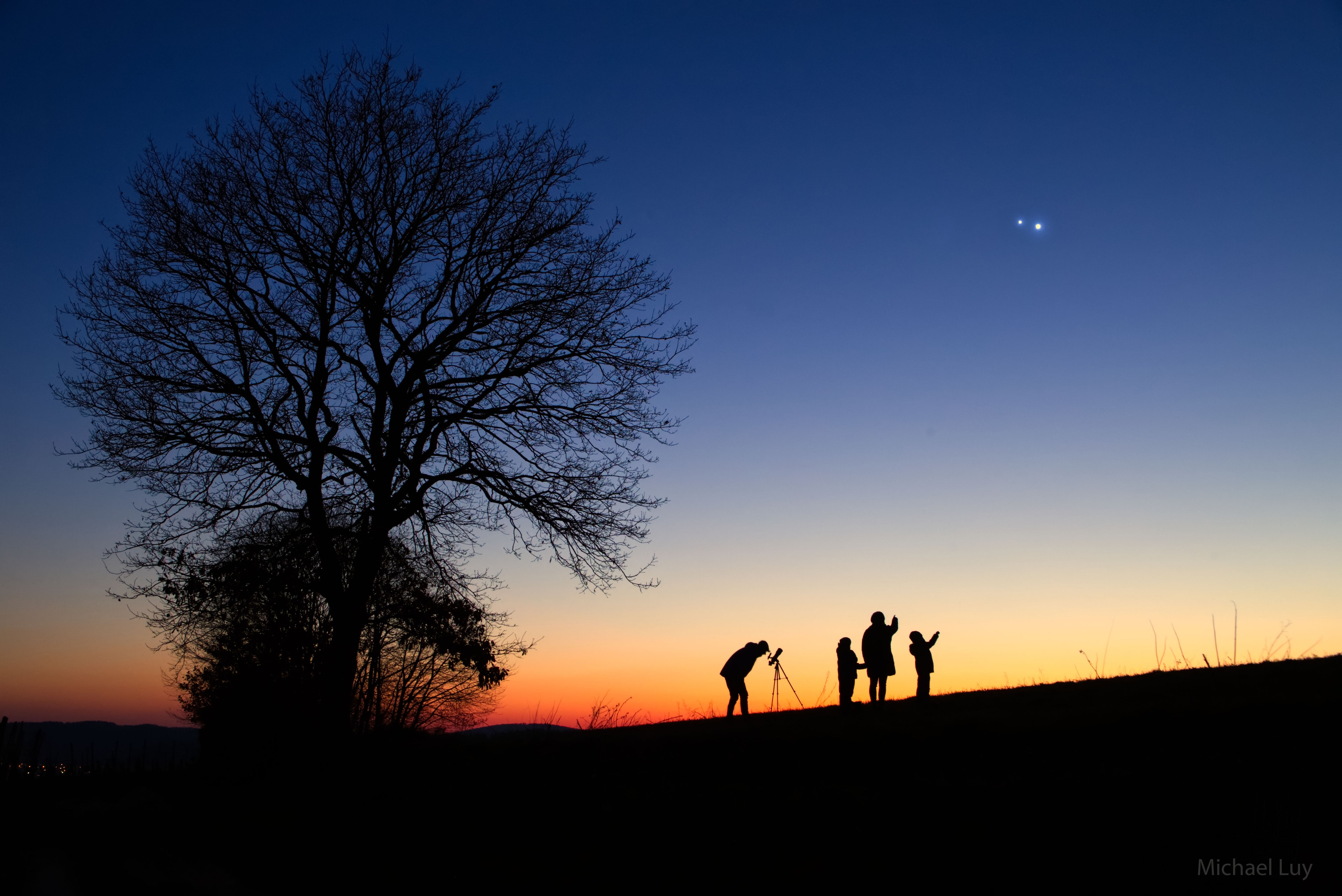 This was a sky to show the kids. Early this month the two brightest planets in the night sky, Jupiter and Venus, appeared to converge. At their closest, the two planets were separated by only about the angular width of the full moon. The spectacle occurred just after sunset and was seen and photographed all across planet Earth. The displayed image was taken near to the time of closest approach from Wiltingen, Germany, and features the astrophotographer, spouse, and their two children.  Of course, Venus remains much closer to both the Sun and the Earth than Jupiter -- the apparent closeness between the planets in the sky of Earth was only angular.  Jupiter and Venus have passed and now appear increasingly far apart. Similar planetary convergence opportunities will eventually arise.  In a few months, for example, Mars and Venus will appear to congregate just as the Sun sets.   Jupiter & Venus Conjunction Gallery: Notable Submissions to APOD