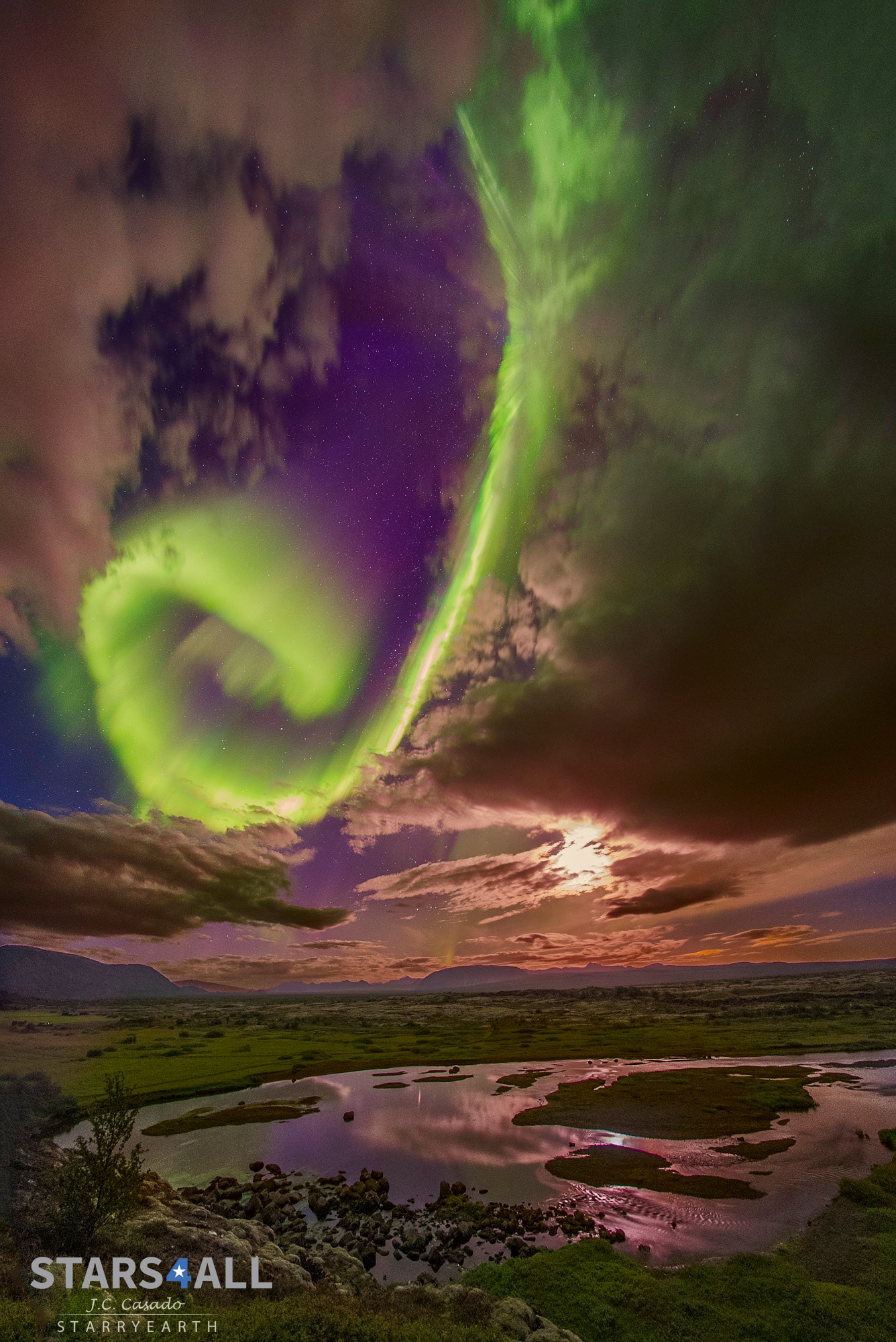 Admire the beauty but fear the beast. The beauty is the aurora overhead, here taking the form of a great green spiral, seen between picturesque clouds with the bright Moon to the side and stars in the background.  The beast is the wave of charged particles that creates the aurora but might, one day, impair civilization.  In 1859, following notable auroras seen all across the globe, a pulse of charged particles from a coronal mass ejection (CME) associated with a solar flare impacted Earth's magnetosphere so forcefully that it created the Carrington Event. This assault from the Sun compressed the Earth's magnetic field so violently that it created high currents and sparks along telegraph wires, shocking many telegraph operators.  Were a Carrington-class event to impact the Earth today, speculation holds that damage might occur to global power grids and electronics on a scale never yet experienced.  The featured aurora was imaged in 2016 over Thingvallavatn Lake in Iceland, a lake that partly fills a fault that divides Earth's large Eurasian and North American tectonic plates.   Almost Hyperspace: Random APOD Generator