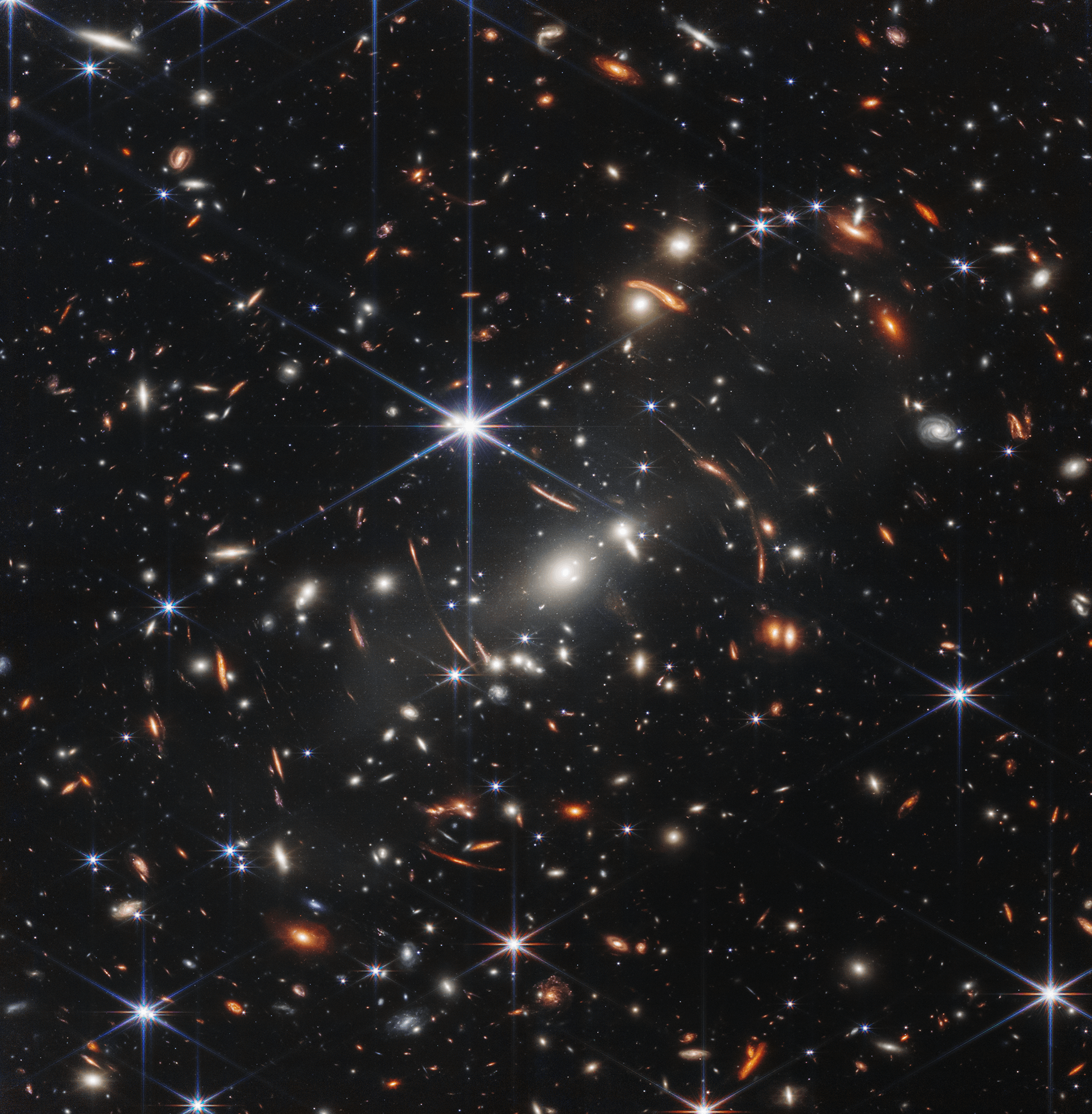 This stunning infrared image was released one year ago as the James Webb Space Telescope began its exploration of the cosmos. The view of the early Universe toward the southern constellation Volans was achieved in 12.5 hours of exposure with Webb's NIRCam instrument. Of course the stars with six spikes are well within our own Milky Way. Their diffraction pattern is characteristic of Webb's 18 hexagonal mirror segments operating together as a single 6.5 meter diameter primary mirror. The thousands of galaxies flooding the field of view are members of the distant galaxy cluster SMACS0723-73, some 4.6 billion light-years away. Luminous arcs that seem to infest the deep field are even more distant galaxies though. Their images are distorted and magnified by the dark matter dominated mass of the galaxy cluster, an effect known as gravitational lensing. Analyzing light from two separate arcs below the bright spiky star, Webb's NIRISS instrument indicates the arcs are both images of the same background galaxy. And that galaxy's light took about 9.5 billion years to reach the James Webb Space Telescope.