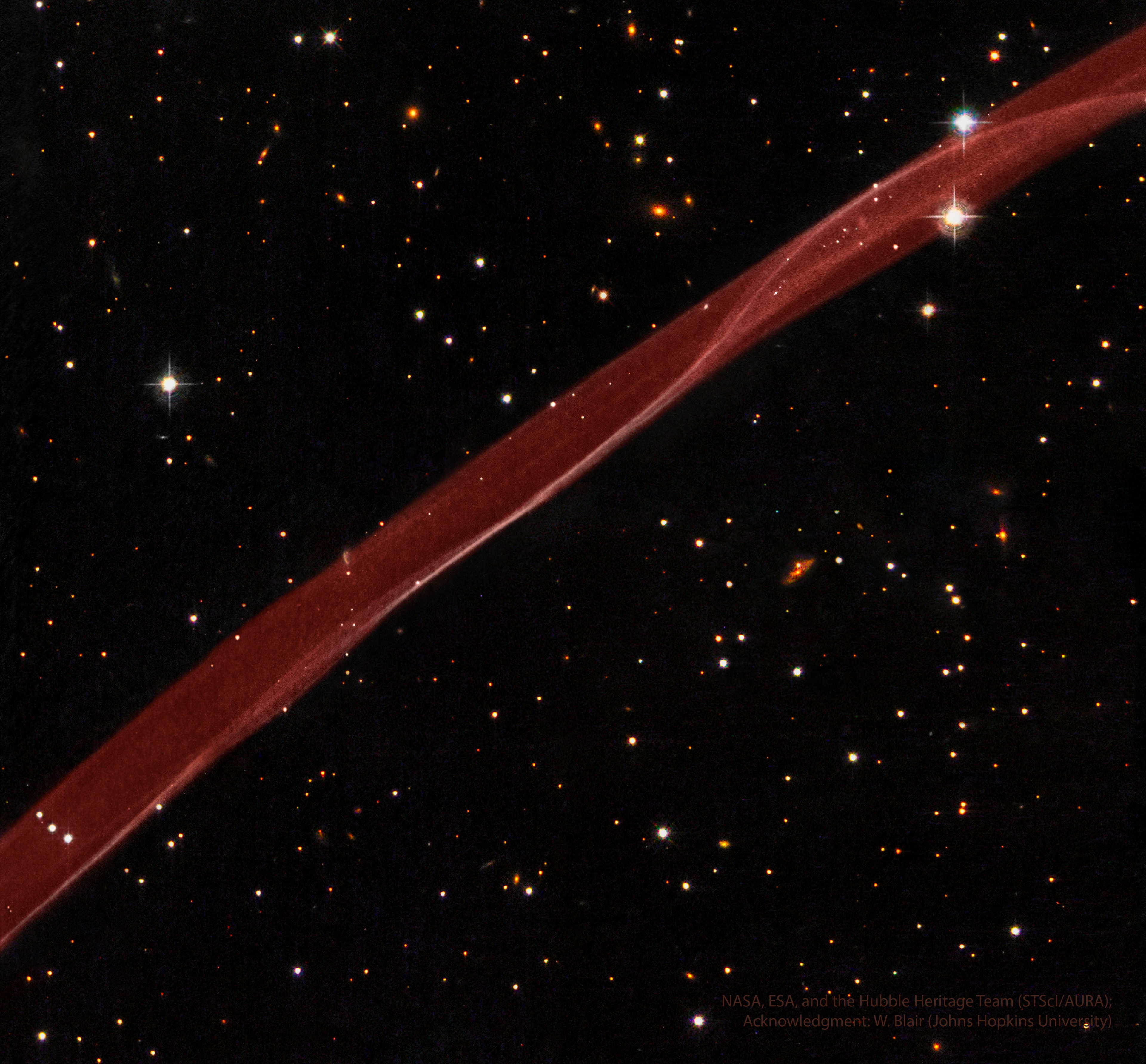 What created this unusual space ribbon?  The answer: one of the most violent explosions ever witnessed by ancient humans. Back in the year 1006 AD, light reached Earth from a stellar explosion in the constellation of the Wolf (Lupus), creating a "guest star" in the sky that appeared brighter than Venus and lasted for over two years. The supernova, now cataloged at SN 1006, occurred about 7,000 light years away and has left a large remnant that continues to expand and fade today.  Pictured here is a small part of that expanding supernova remnant dominated by a thin and outwardly moving shock front that heats and ionizes surrounding ambient gas. The supernova remnant SN 1006 now has a diameter of nearly 60 light years.